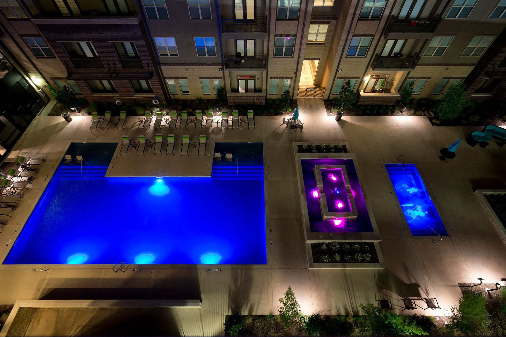 A large swimming pool is lit up at night in front of a building.