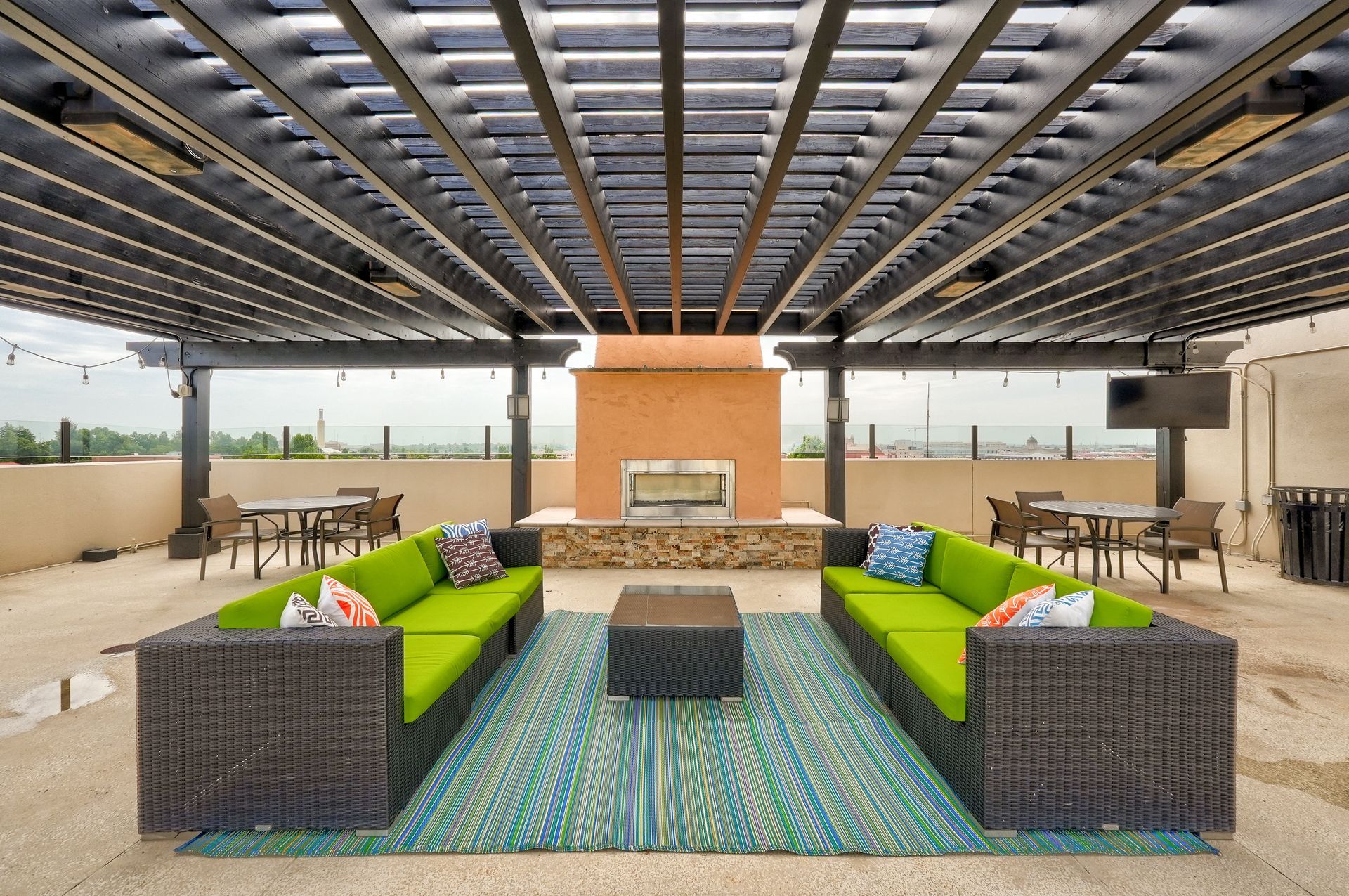 A patio with green couches and a fireplace under a pergola.