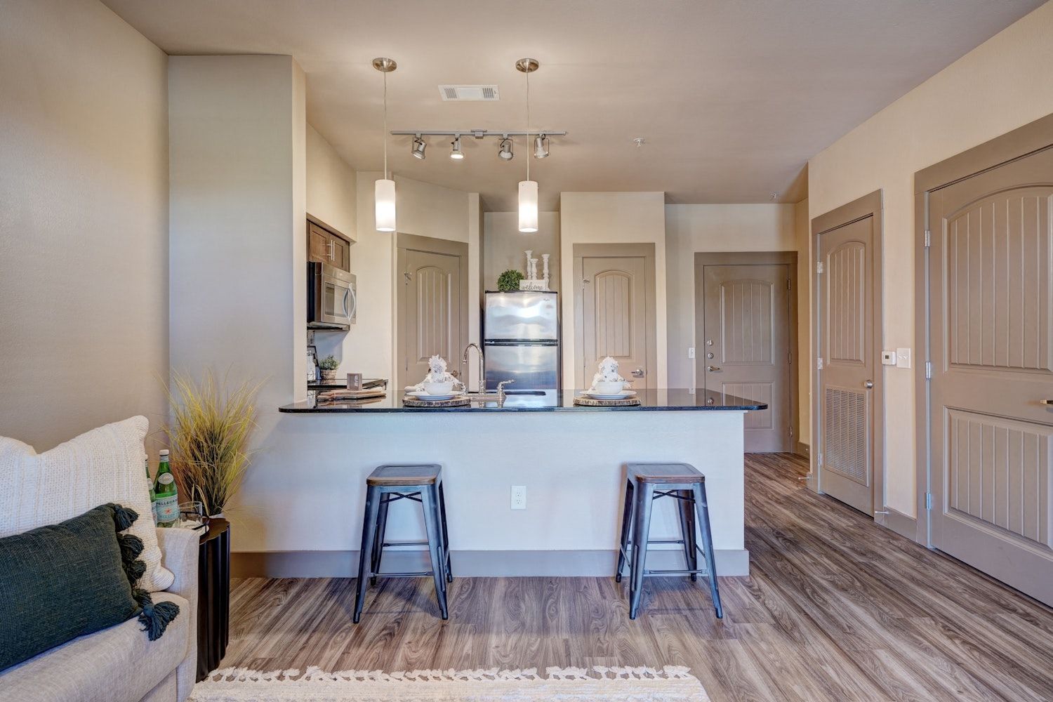 A living room with a couch, stools, and a kitchen.