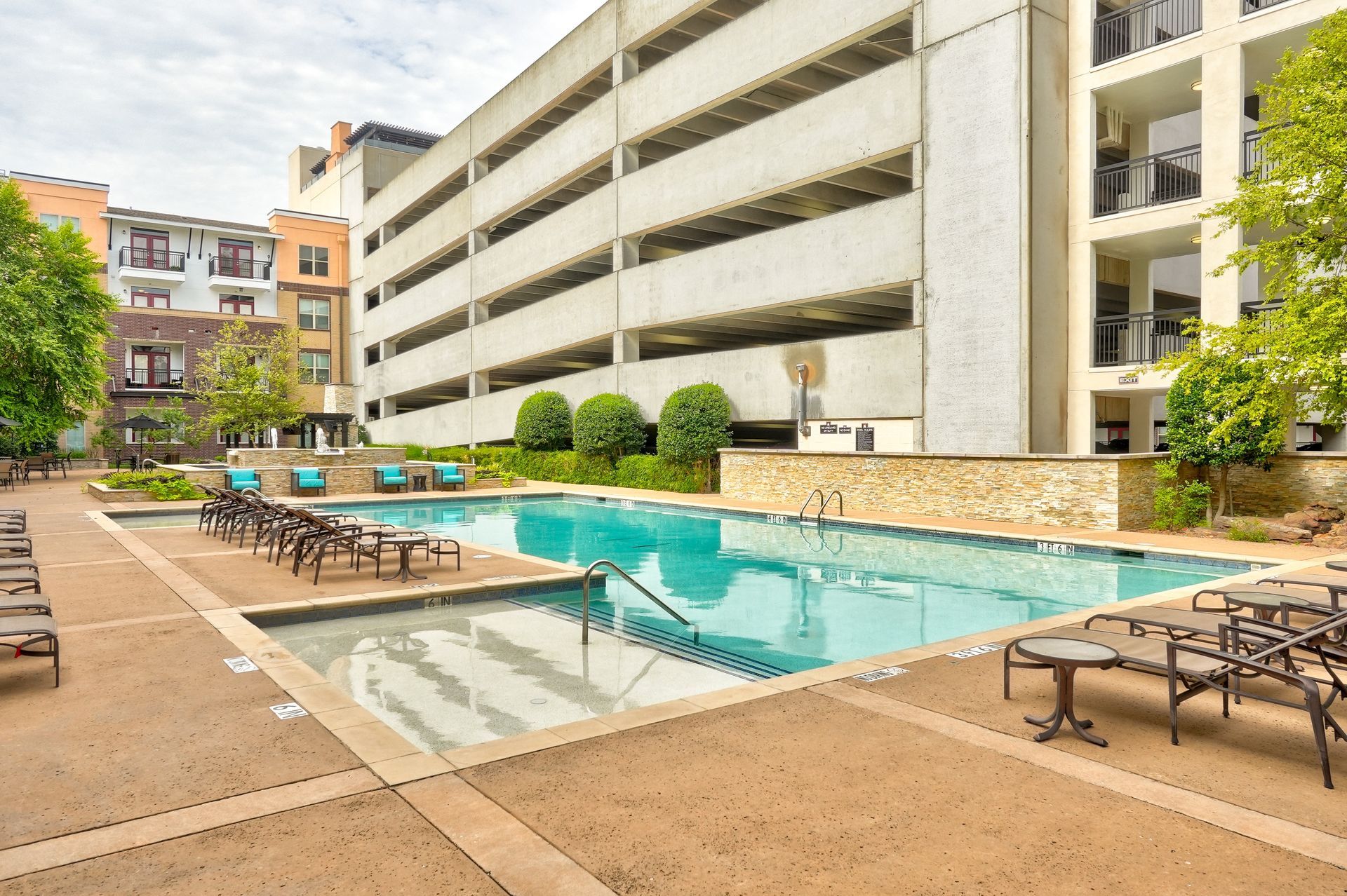 A large swimming pool surrounded by chairs and tables in front of a building.
