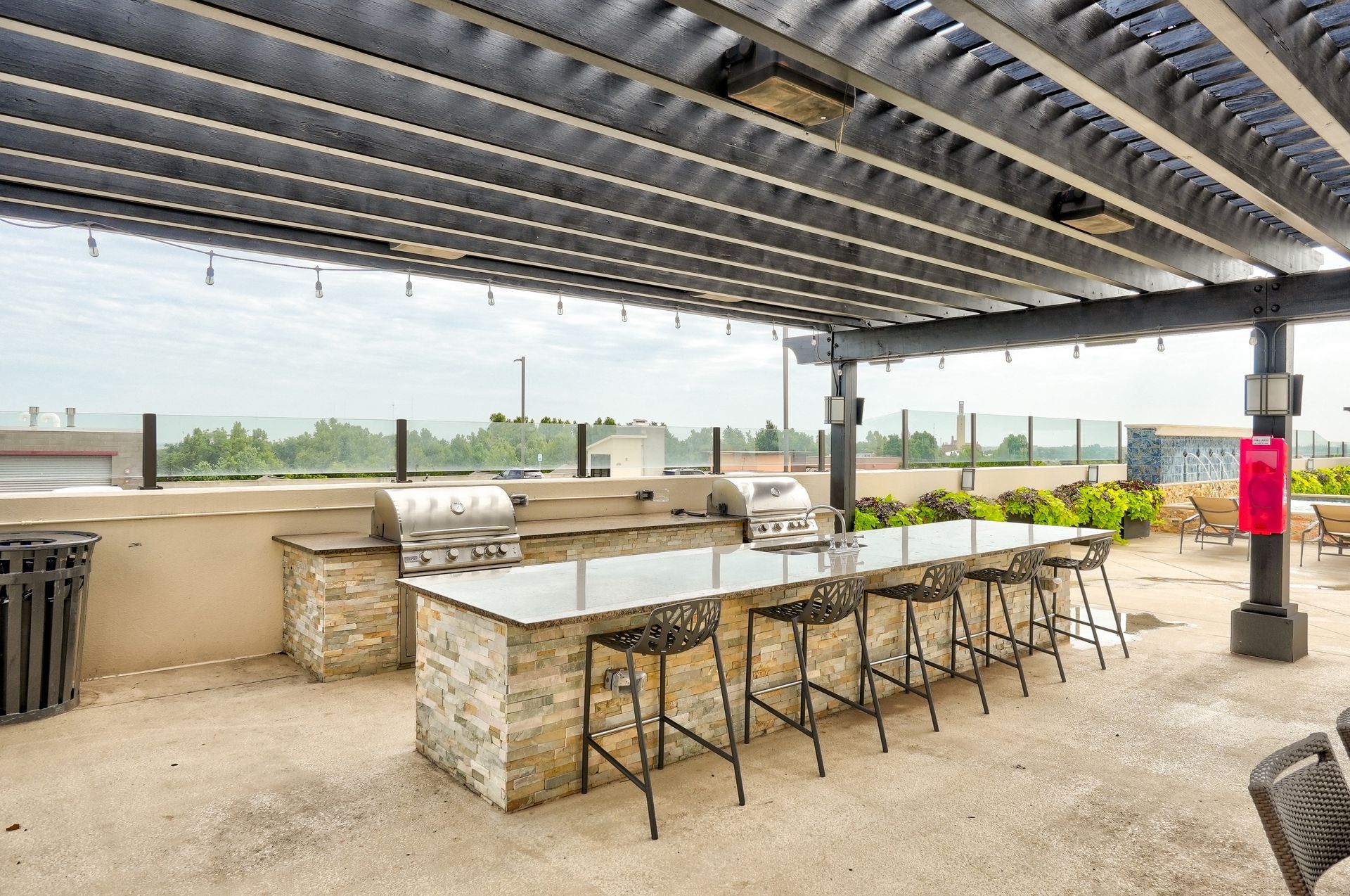 A large outdoor kitchen with stools and grills under a pergola.