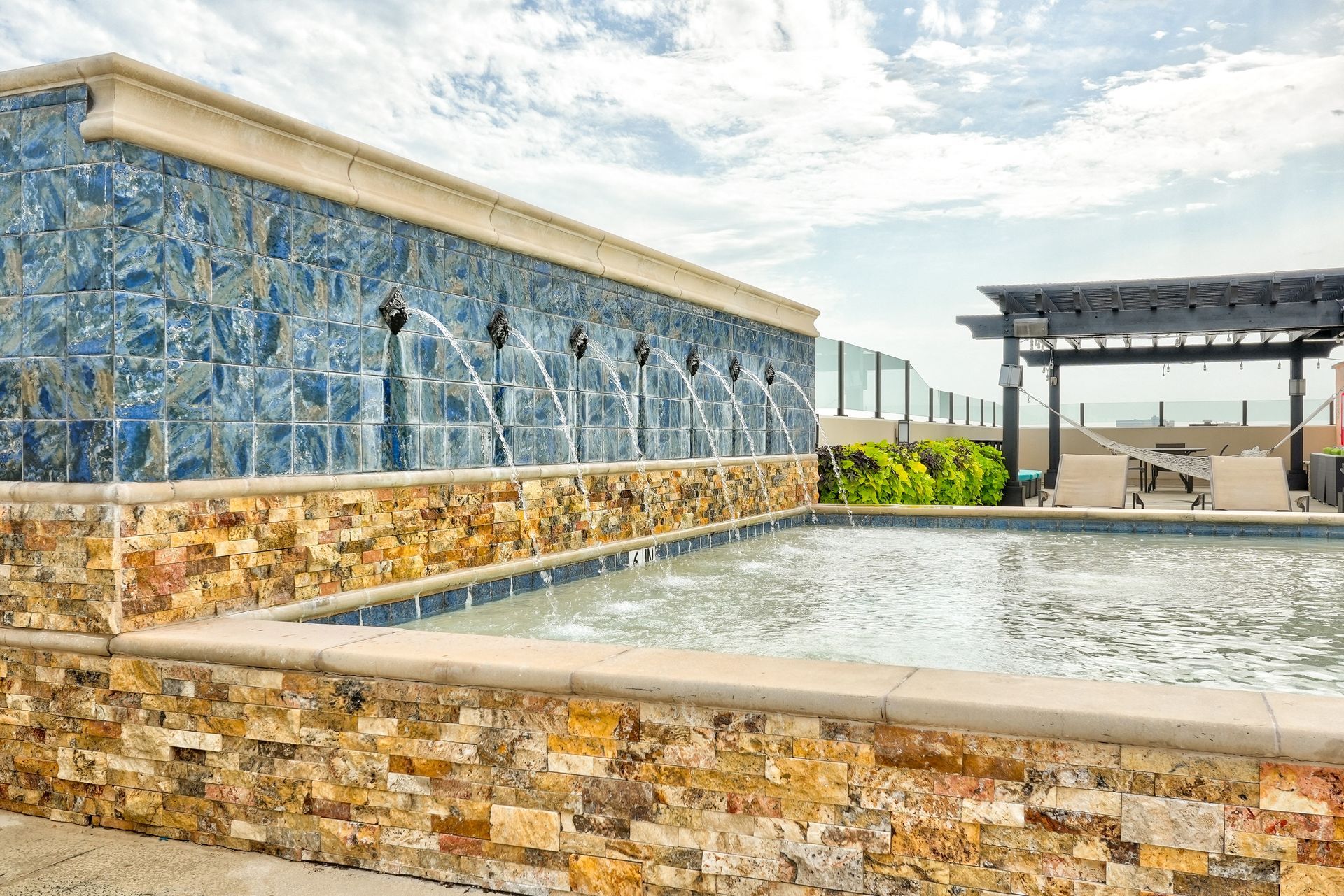 A large swimming pool surrounded by a stone wall and a fountain.