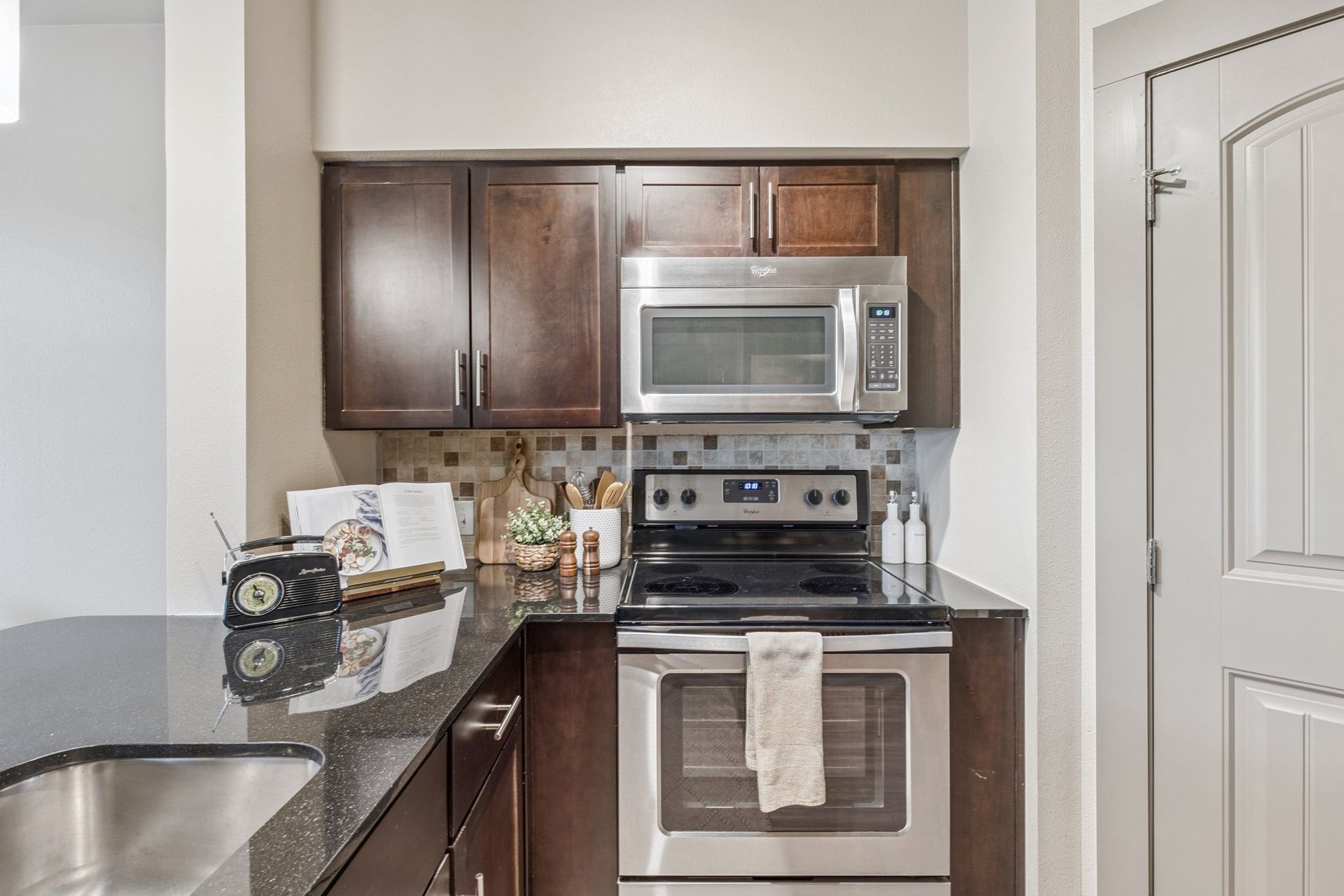 Kitchen with dark wood cabinets, stainless steel appliances, and black countertop.