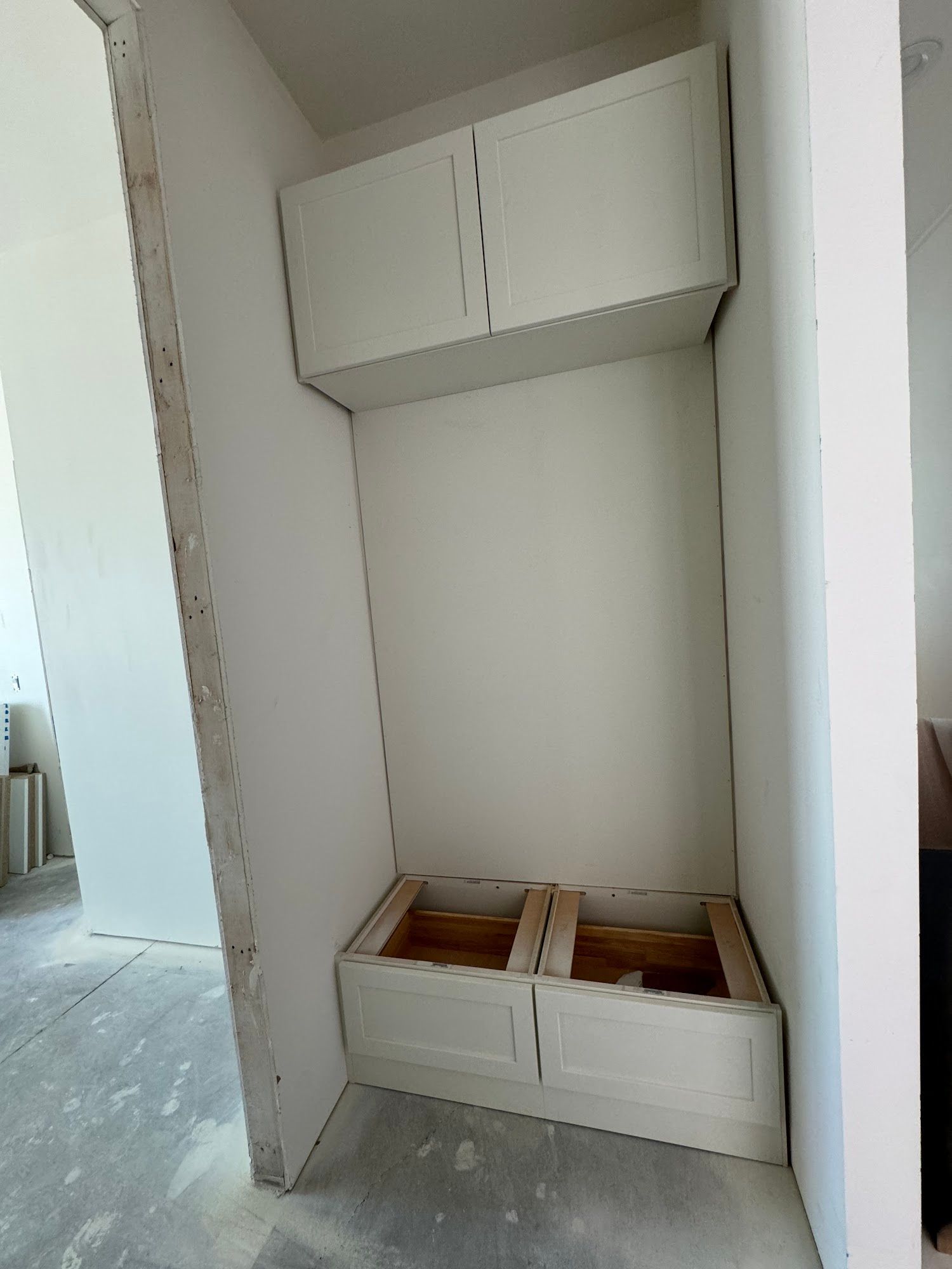 Kitchen cabinets, unfinished installation. Brown cabinets against white walls, light wood floor.