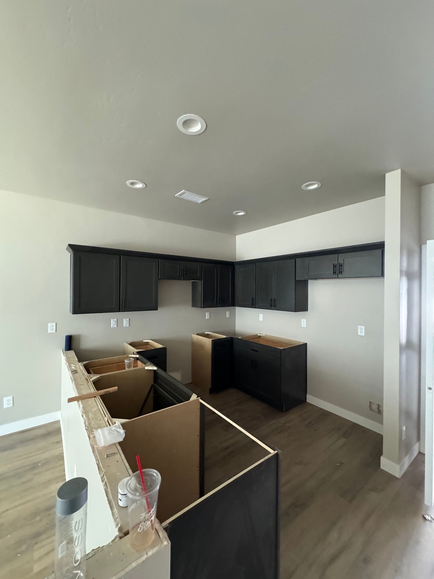 Unfinished kitchen with dark cabinets, light-colored walls, and wooden floors; construction phase.