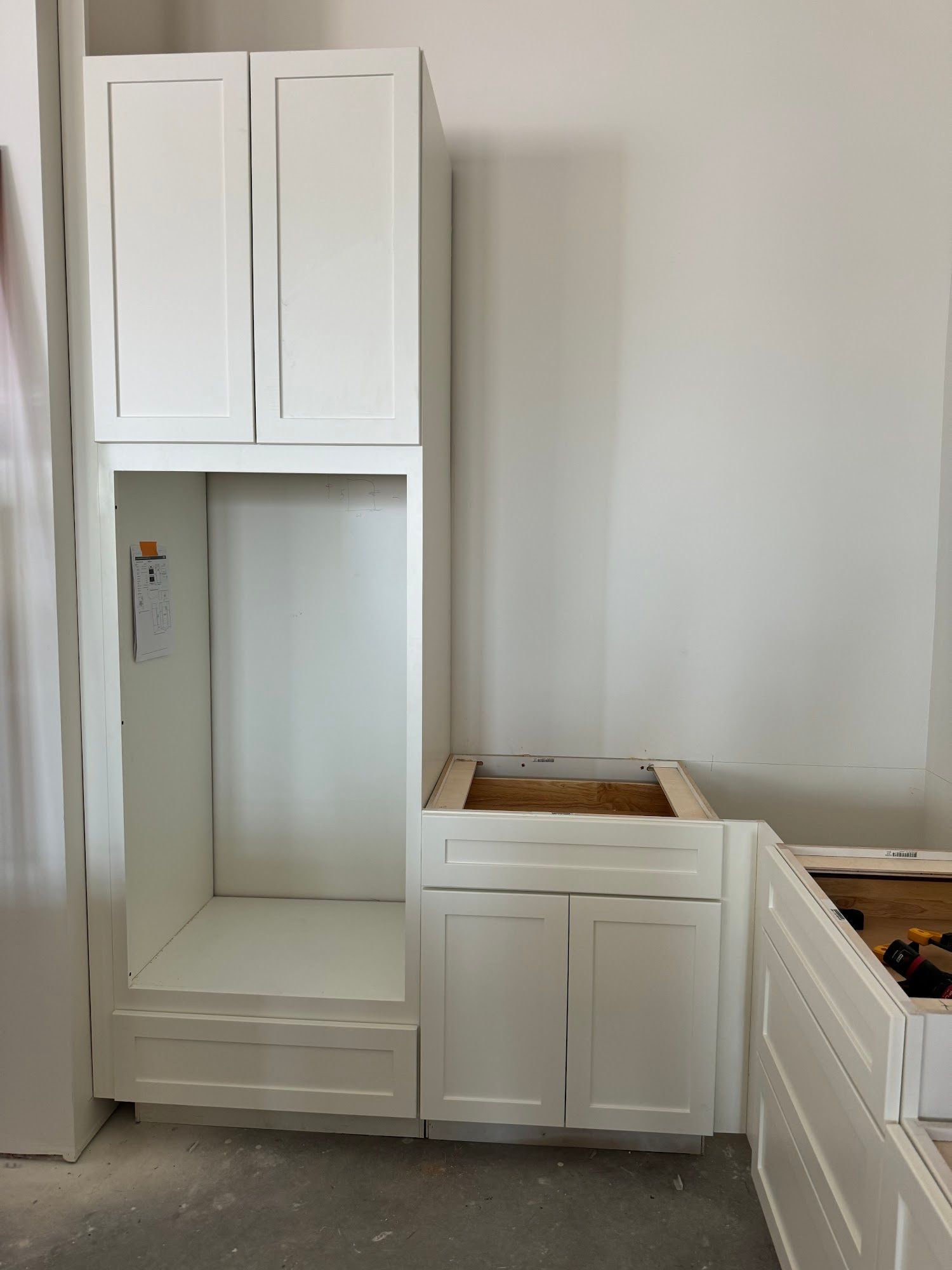 White kitchen cabinets, unfinished installation. Includes an oven cabinet and base cabinets, against a white wall.