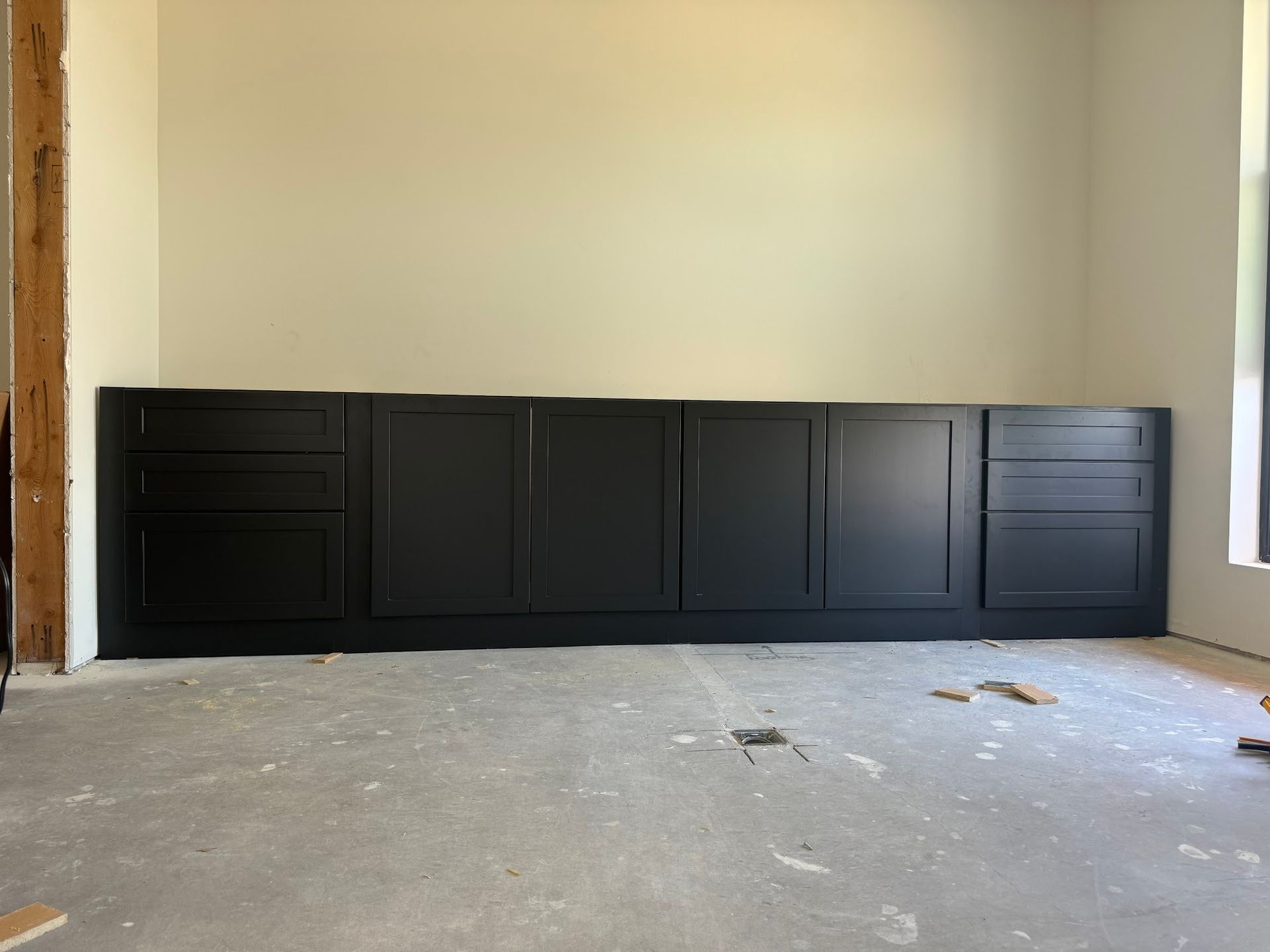 Black cabinets installed along a wall in an unfinished room.