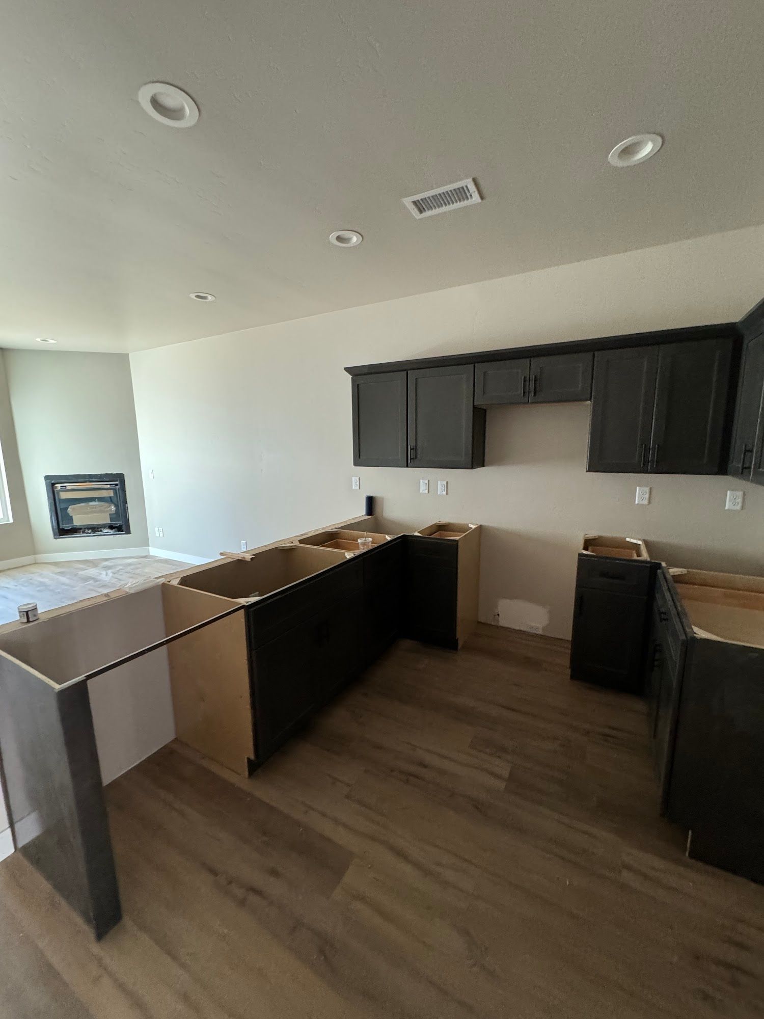 Kitchen under construction with dark cabinets, light floors, and a fireplace in the background.