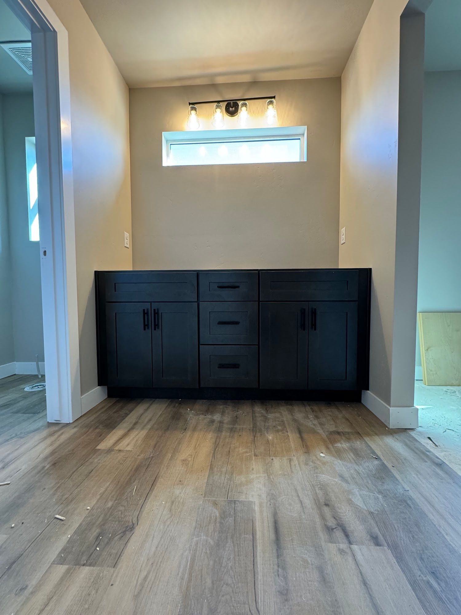 Black bathroom vanity with three drawers and two cabinets, under a light fixture and window.