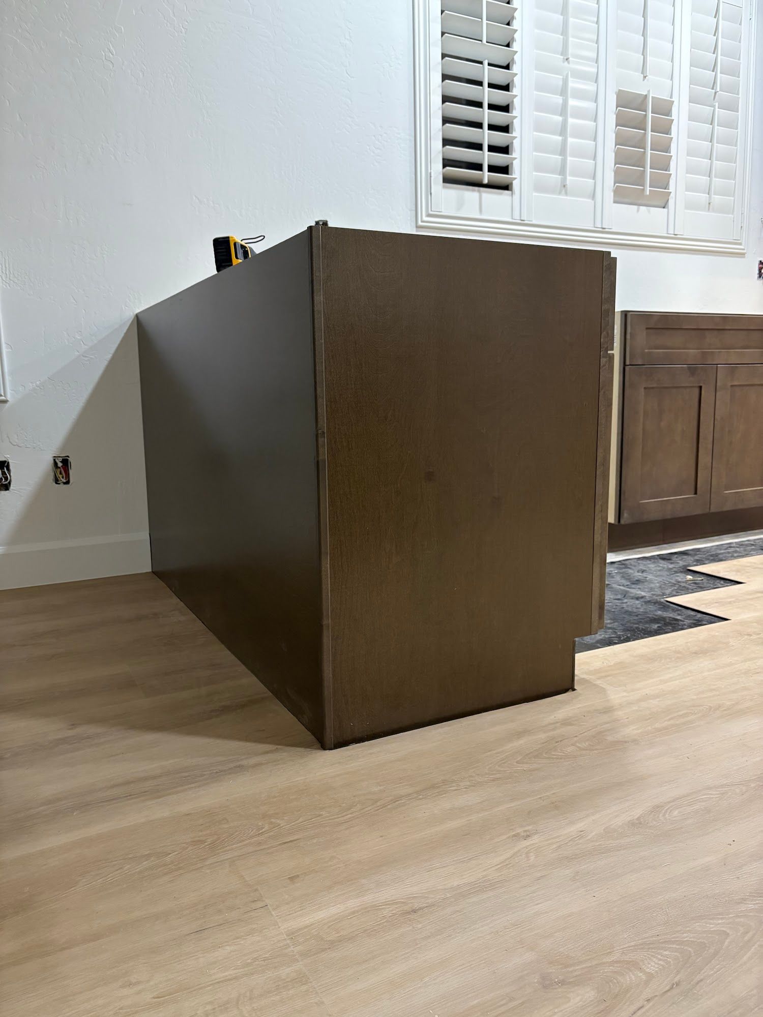 Brown cabinet against a white wall with a window, in a room with light wood floors.
