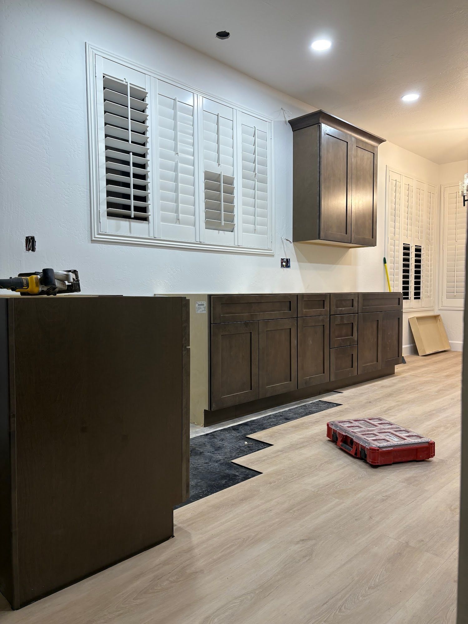 Kitchen renovation: new cabinets, flooring, and window shutters; tools and materials scattered.