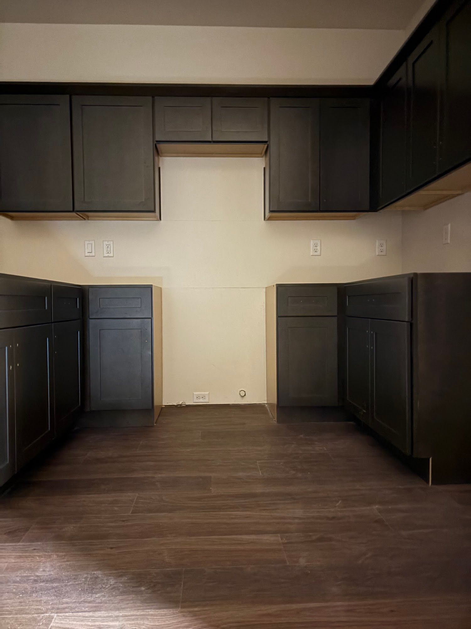 Dark gray kitchen cabinets installed on a wood floor, with a blank wall space for appliances.
