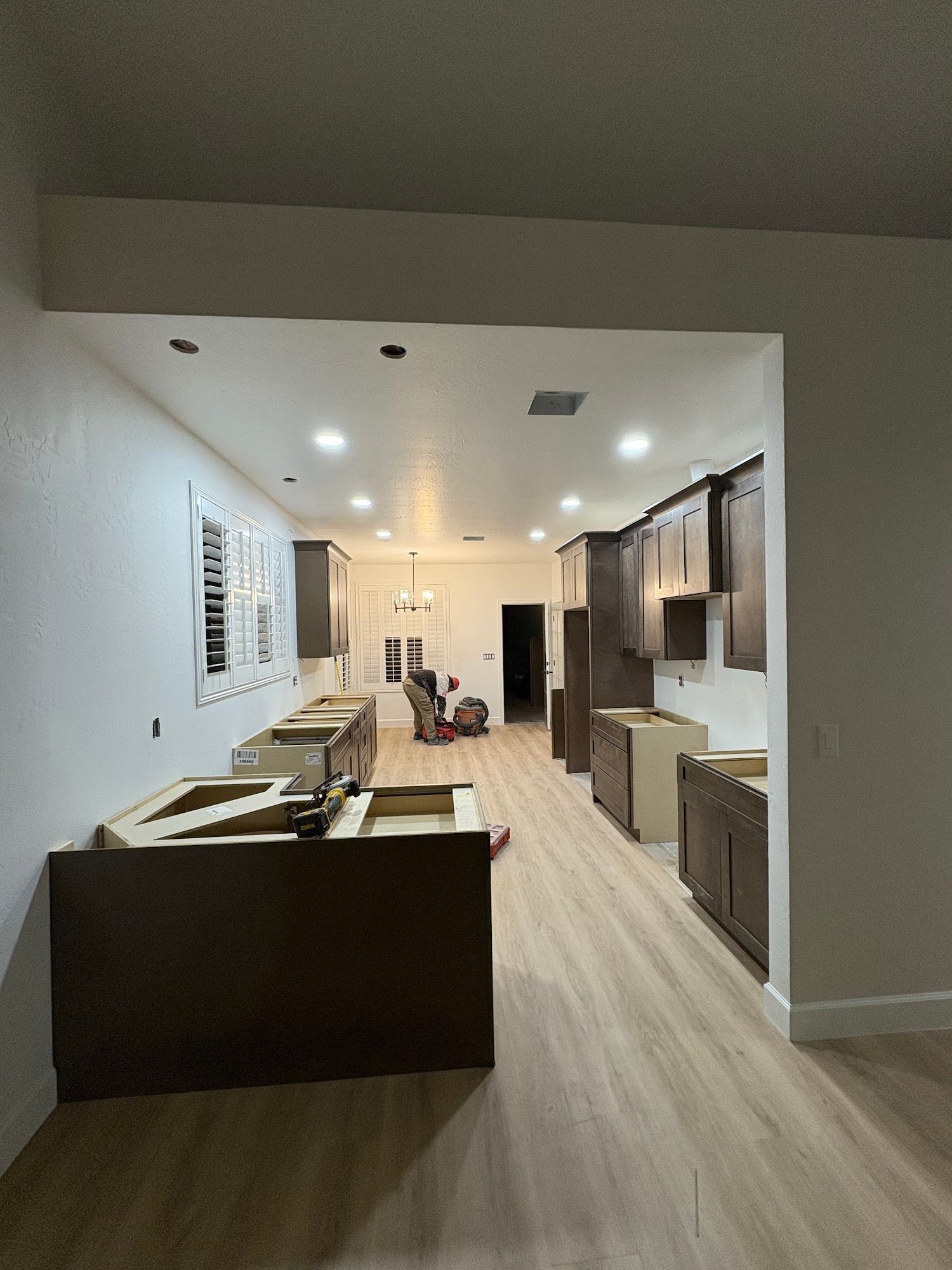 Kitchen remodel in progress: base cabinets and wall cabinets installed. Brown cabinets, light wood floor, white walls.