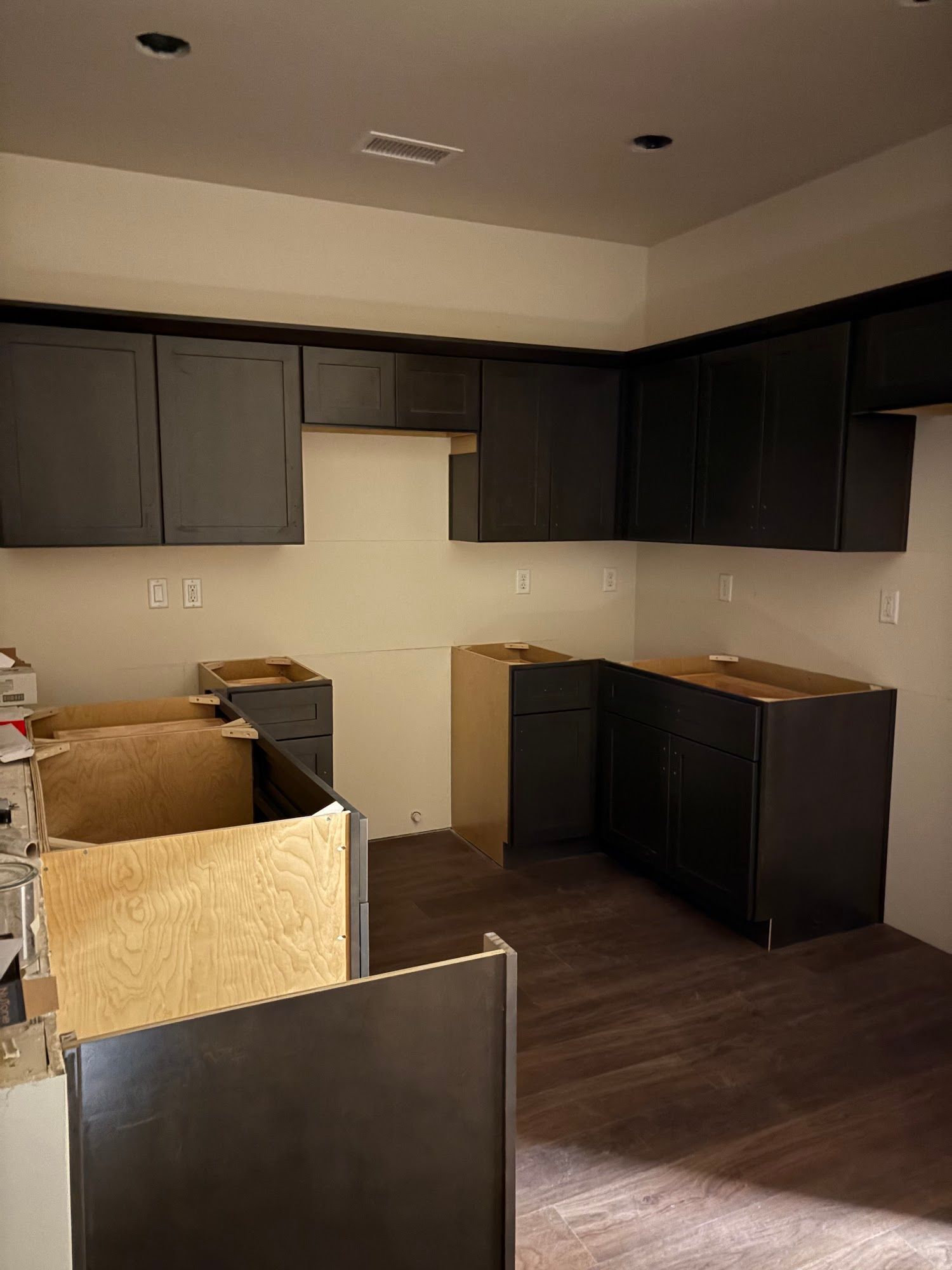 Kitchen under construction with dark cabinets, light walls, and wood flooring.