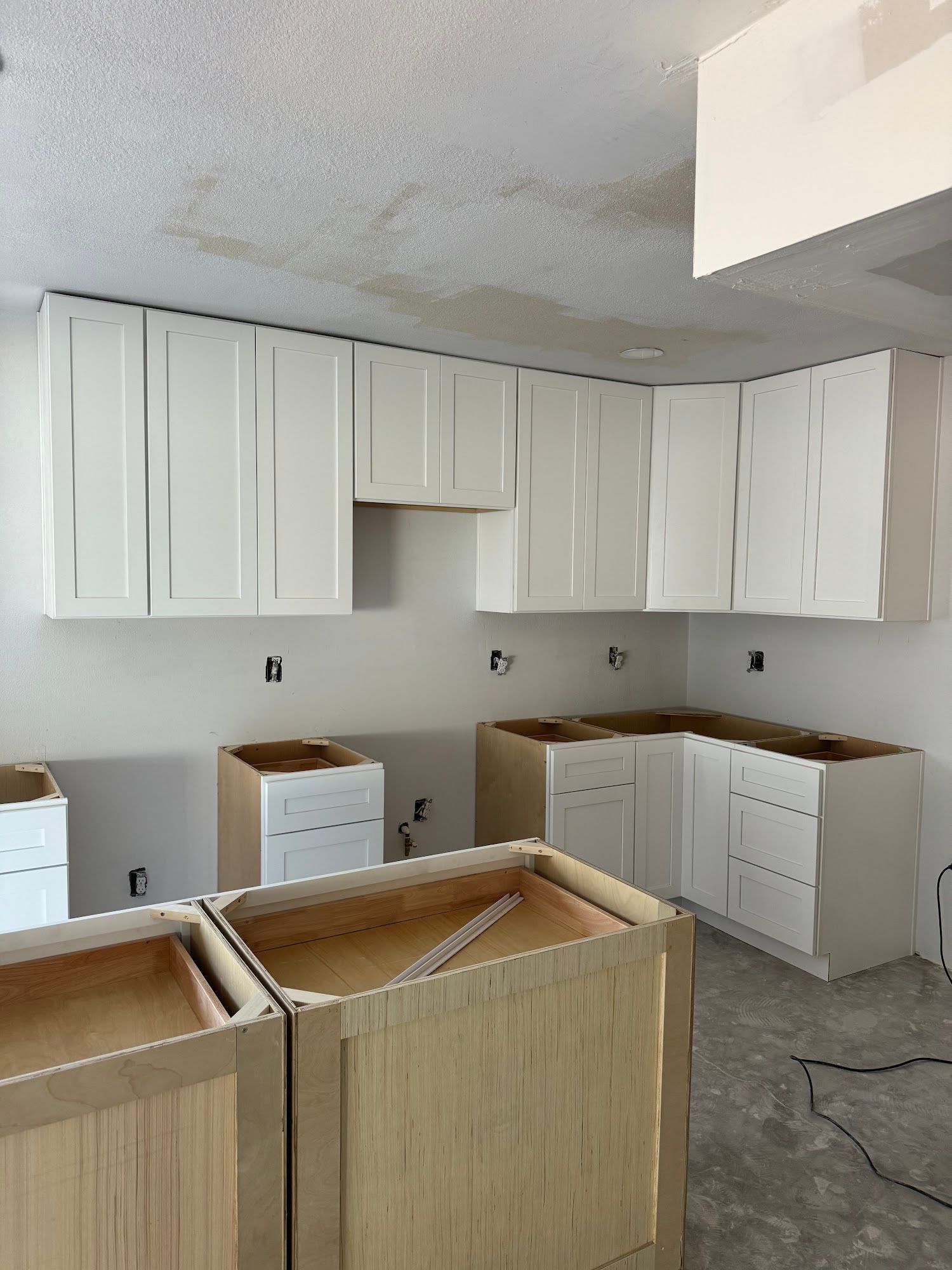 Kitchen under construction with white upper cabinets and unfinished lower cabinets.
