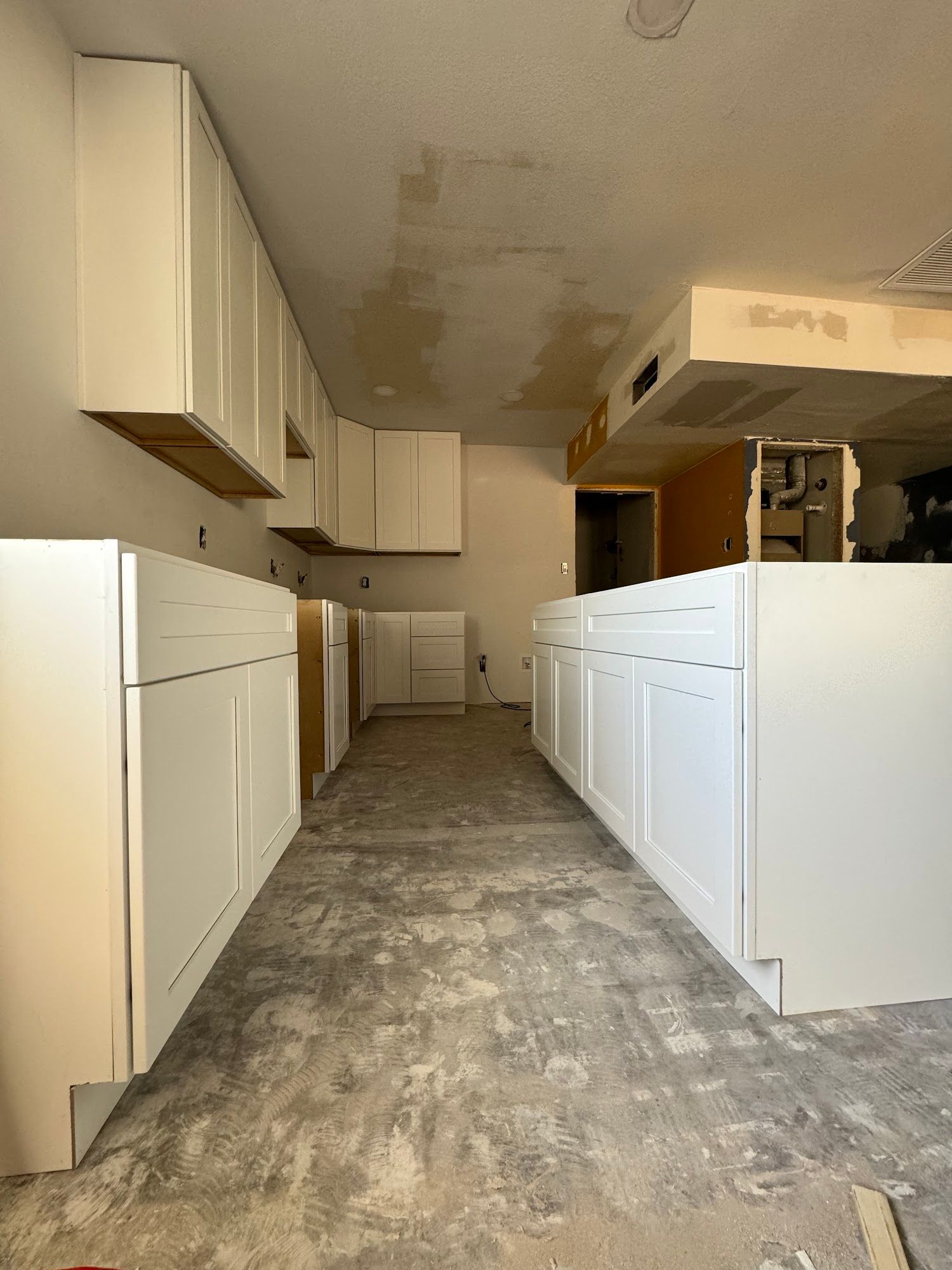 Kitchen under renovation with white cabinets installed on concrete floor.