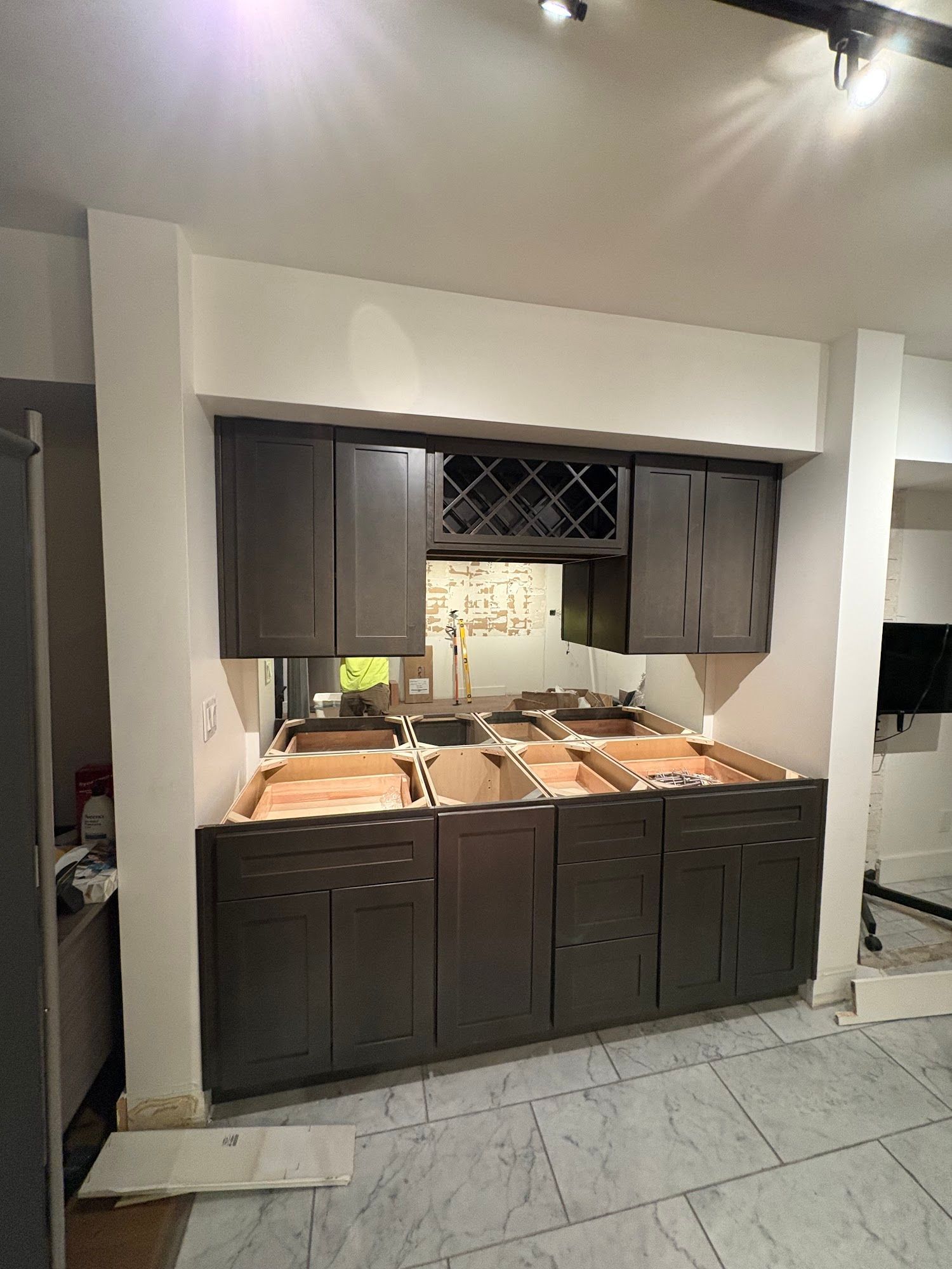 Brown cabinet against a white wall and wooden floor. Window with shutters in the background.
