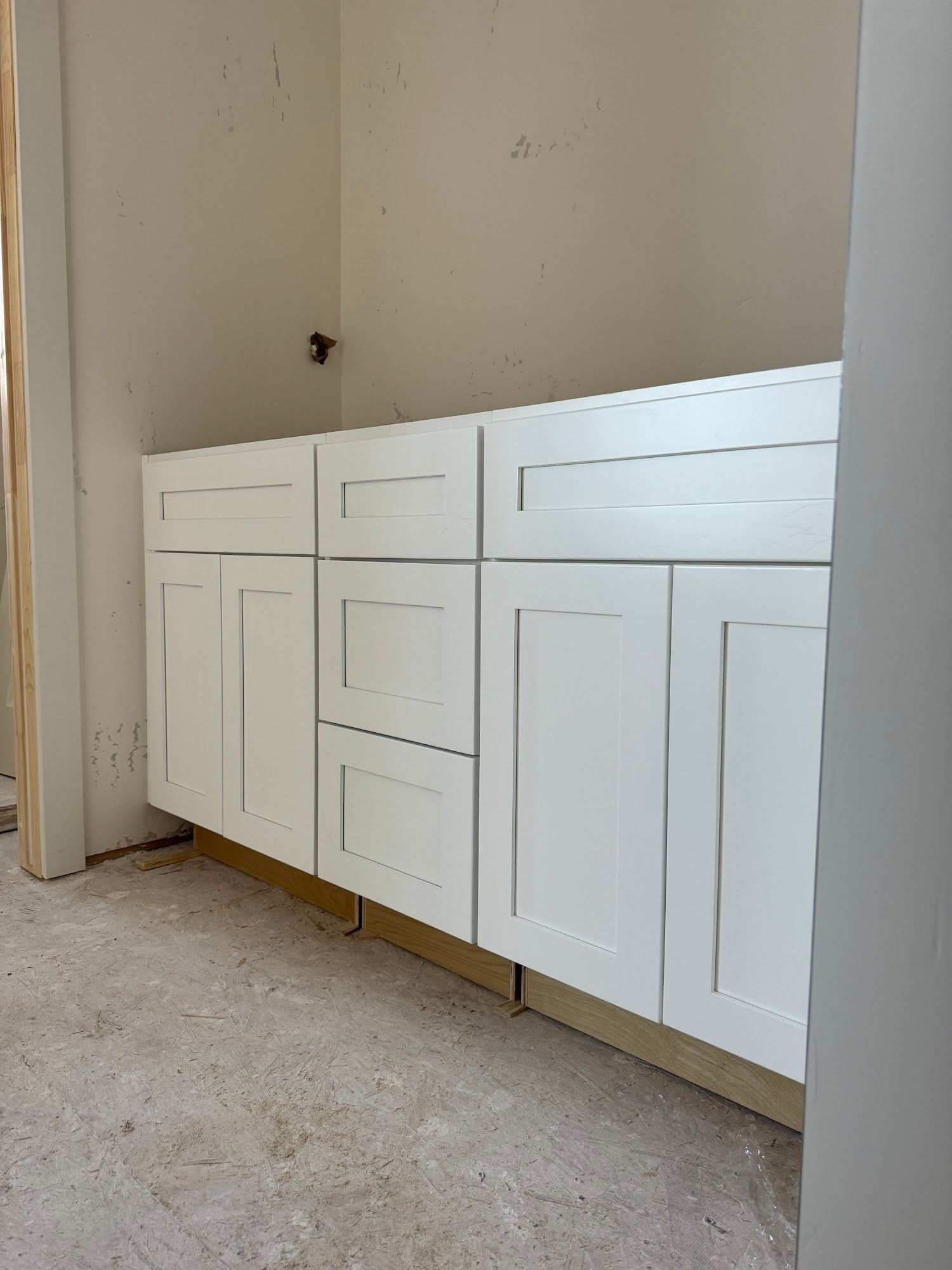 White kitchen cabinets, unfinished installation. Includes an oven cabinet and base cabinets, against a white wall.