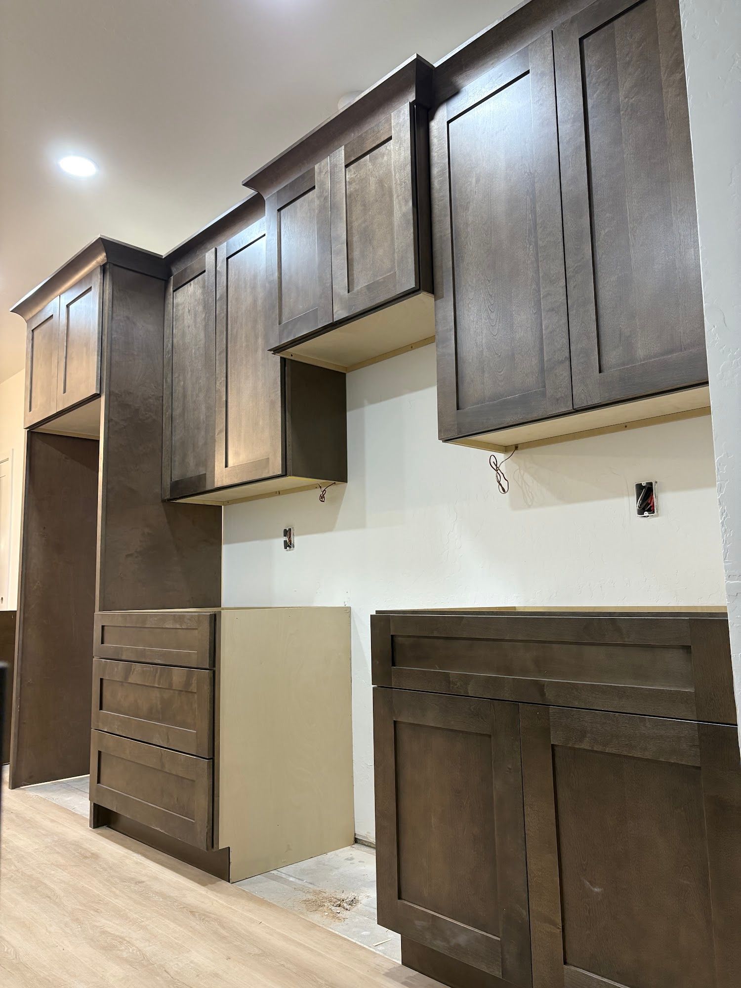 Kitchen cabinets, unfinished installation. Brown cabinets against white walls, light wood floor.