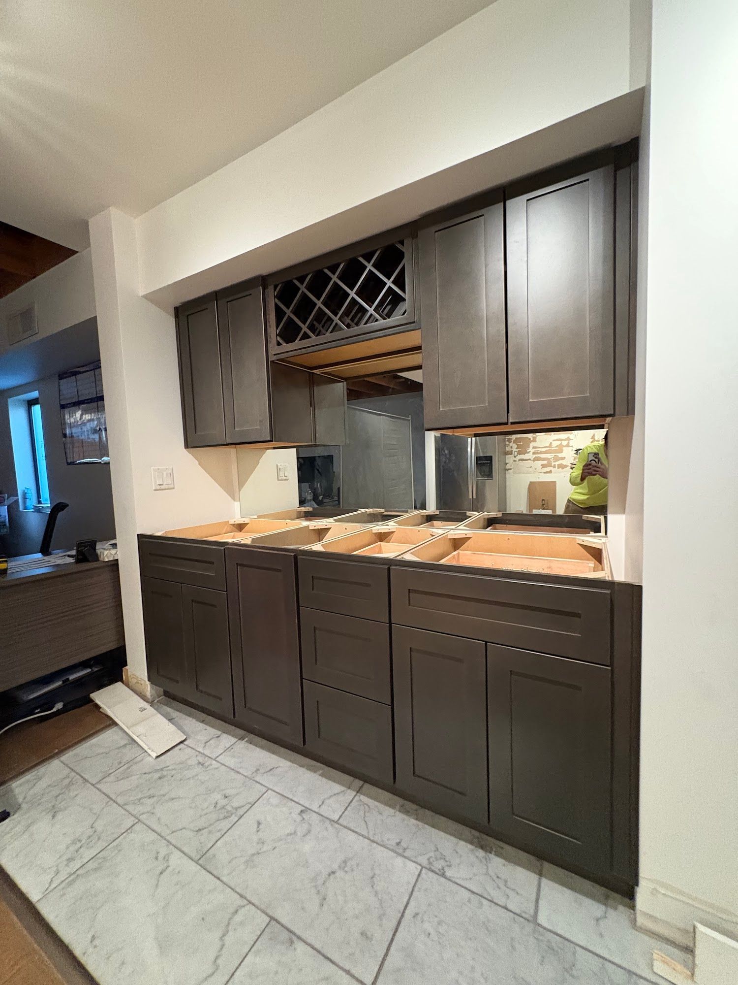 Gray cabinets being installed, with unfinished countertop, wine rack, and a mirror in the center.