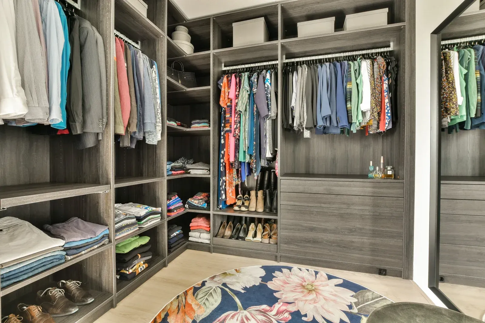 Walk-in closet with gray shelves and rods filled with clothing. A round floral rug sits on the floor.