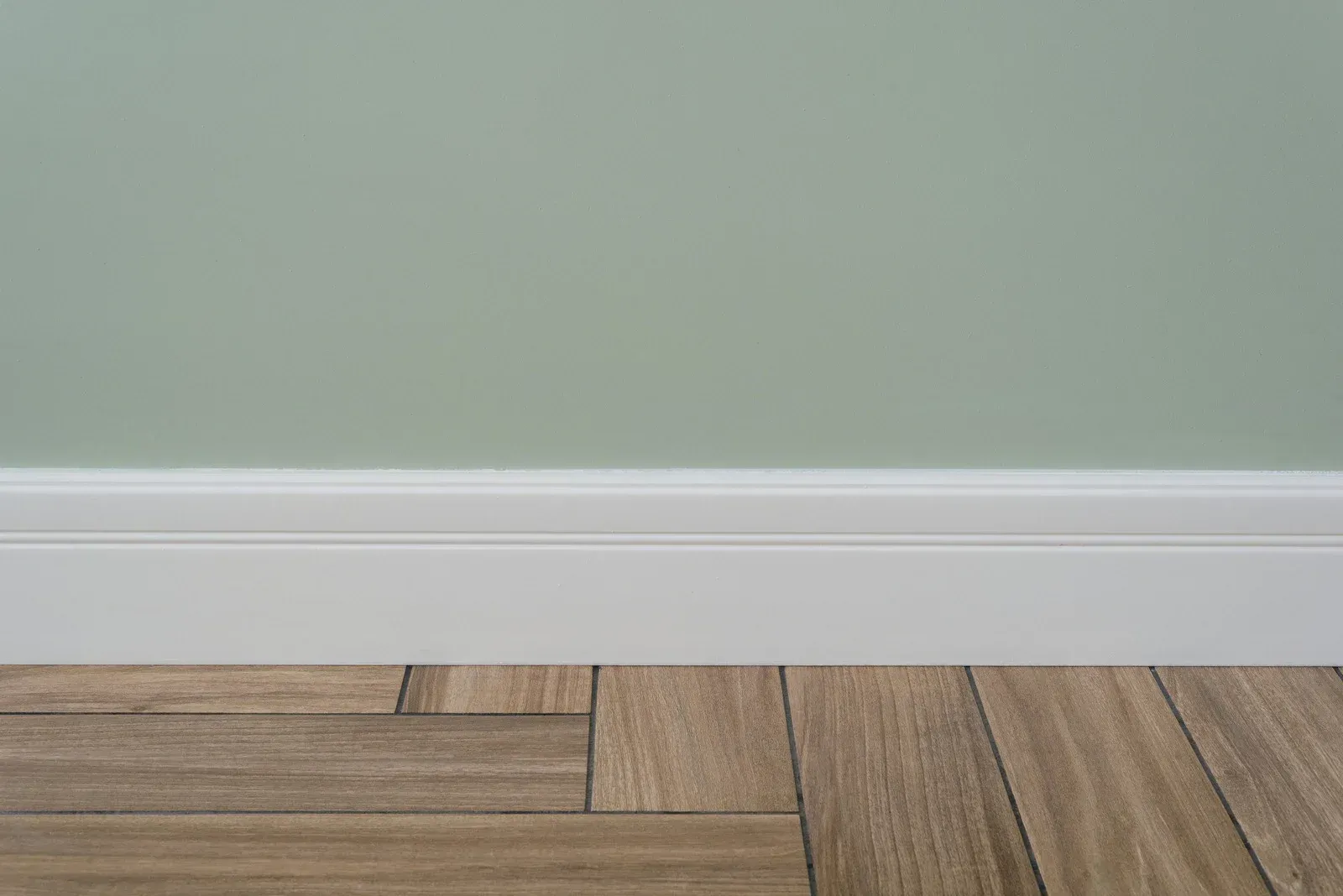 Green wall, white baseboard, and wood-look tile flooring.