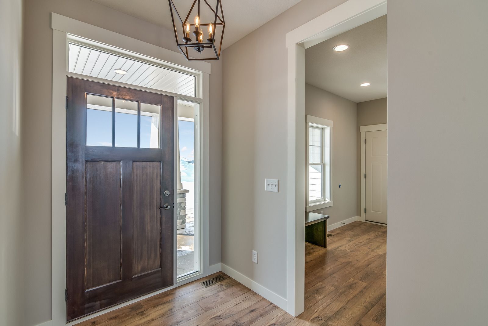 Entryway with staircase, wooden floors, beige walls, white trim, front door, and a table with lamp and flowers.