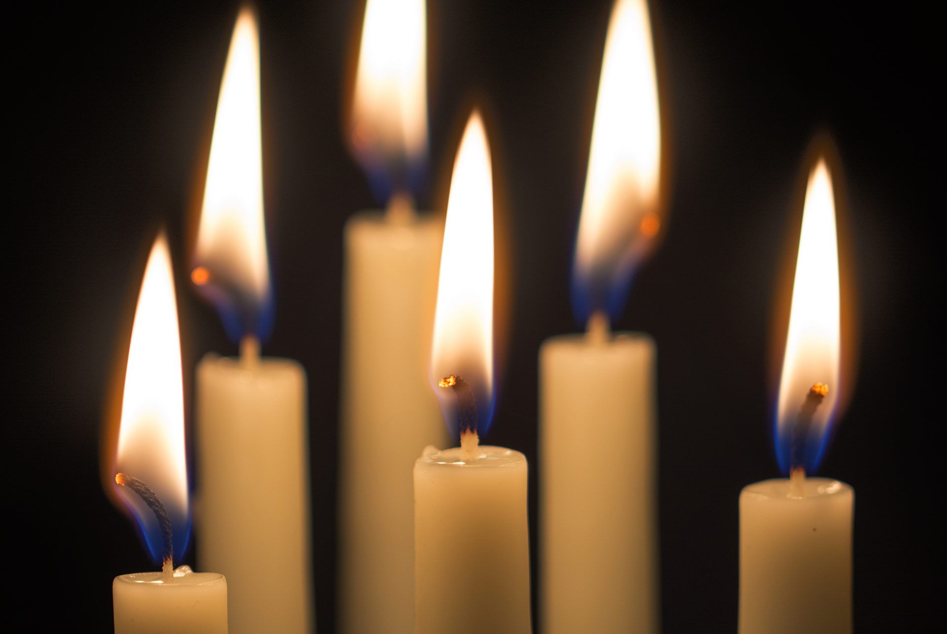 group of six burning candles against a black background, selected focus, narrow depth of field