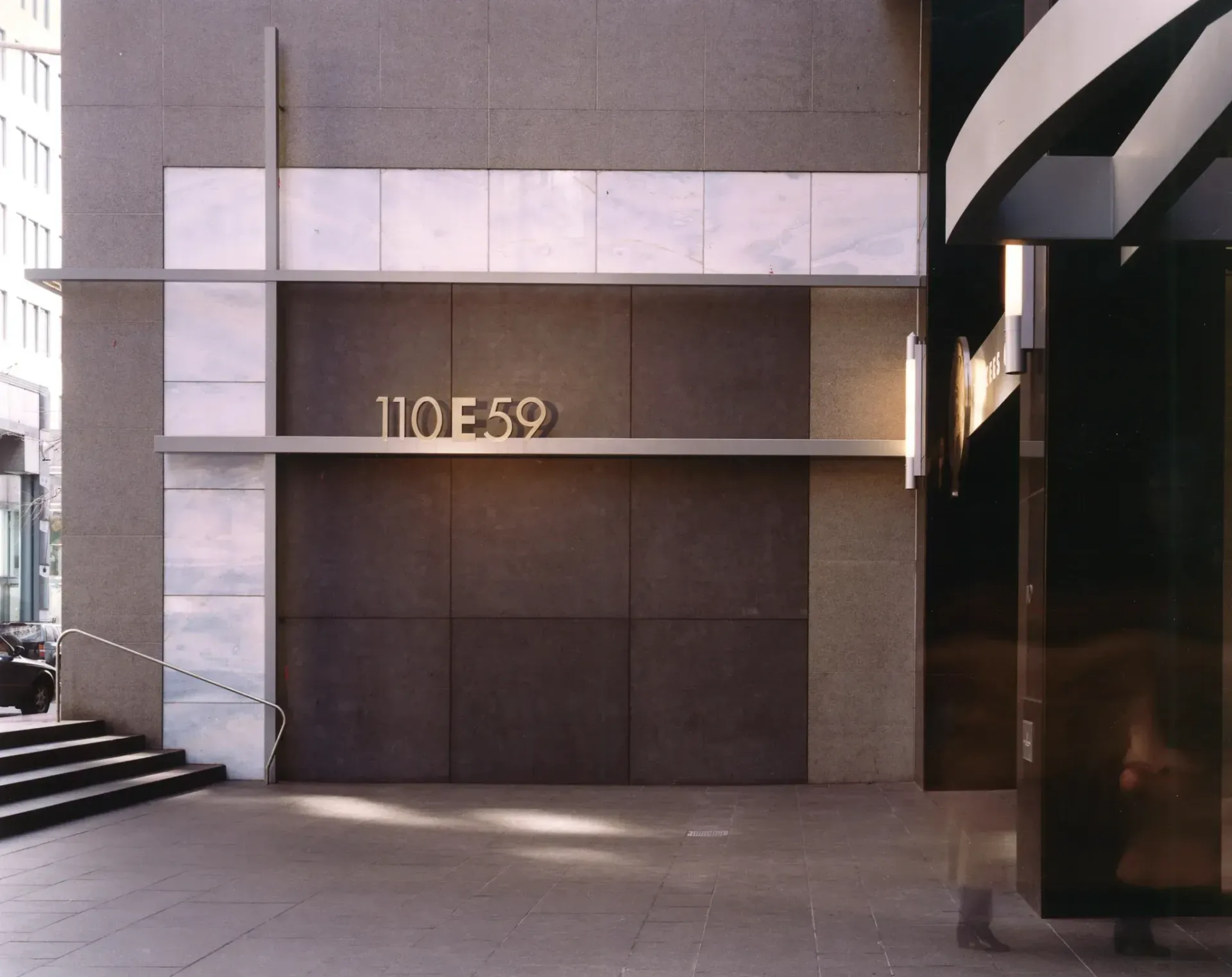 Entrance to 110 E 59 building with a gray facade, brown doors, and marble accents. Metallic sign reading