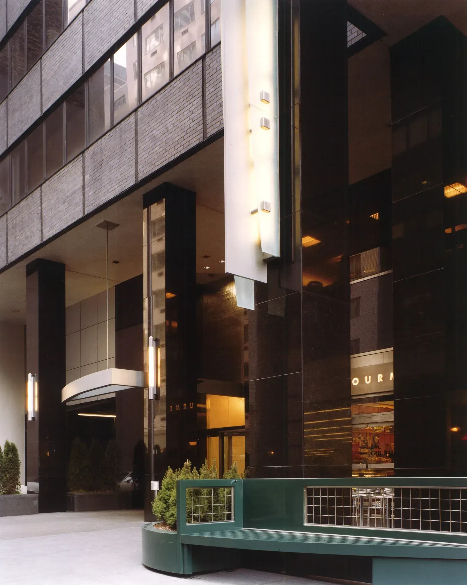 Entrance to a modern building with glossy black pillars, a green bench, and a storefront visible on the right.