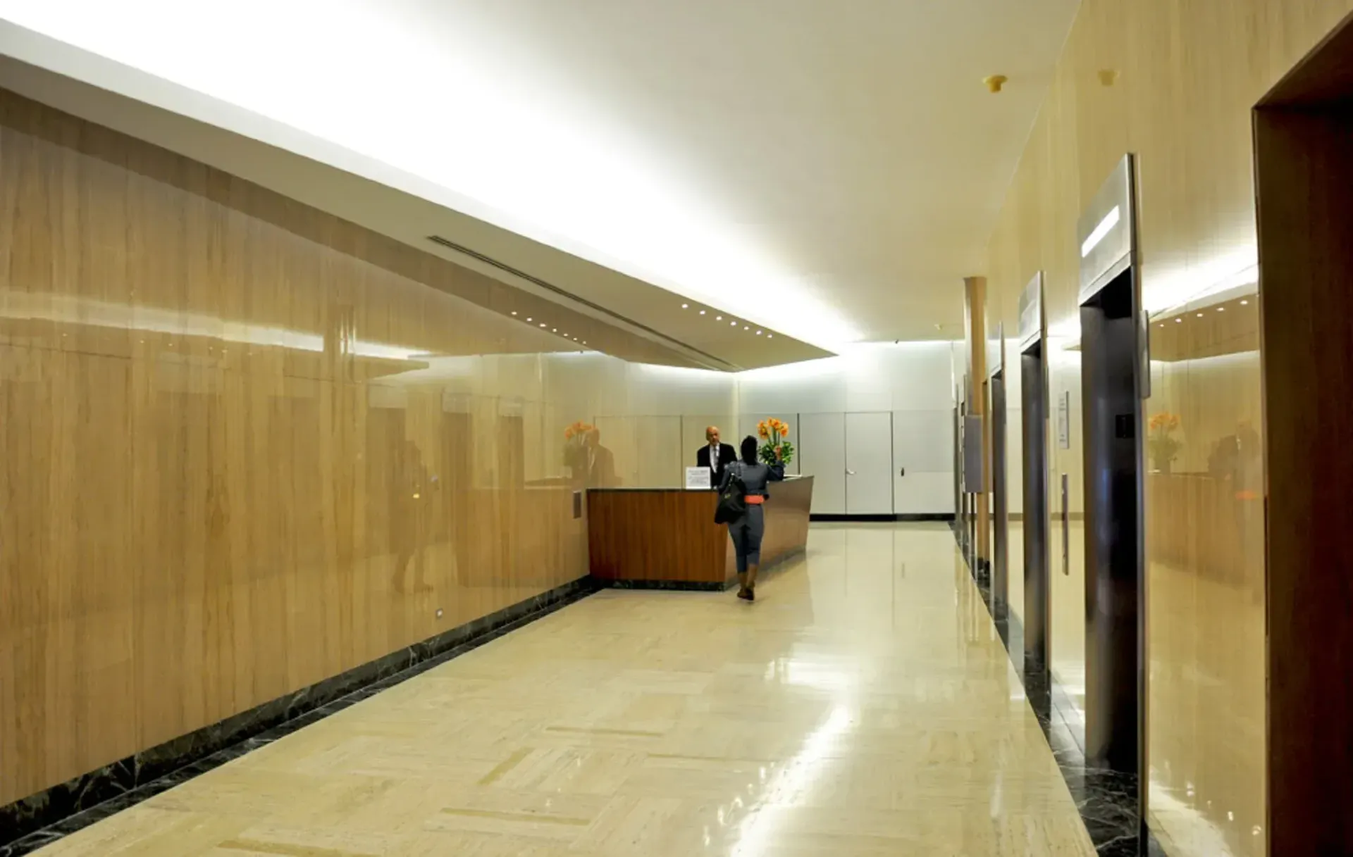 Elevator lobby with wood-paneled walls, a reception desk, and a person walking toward it.