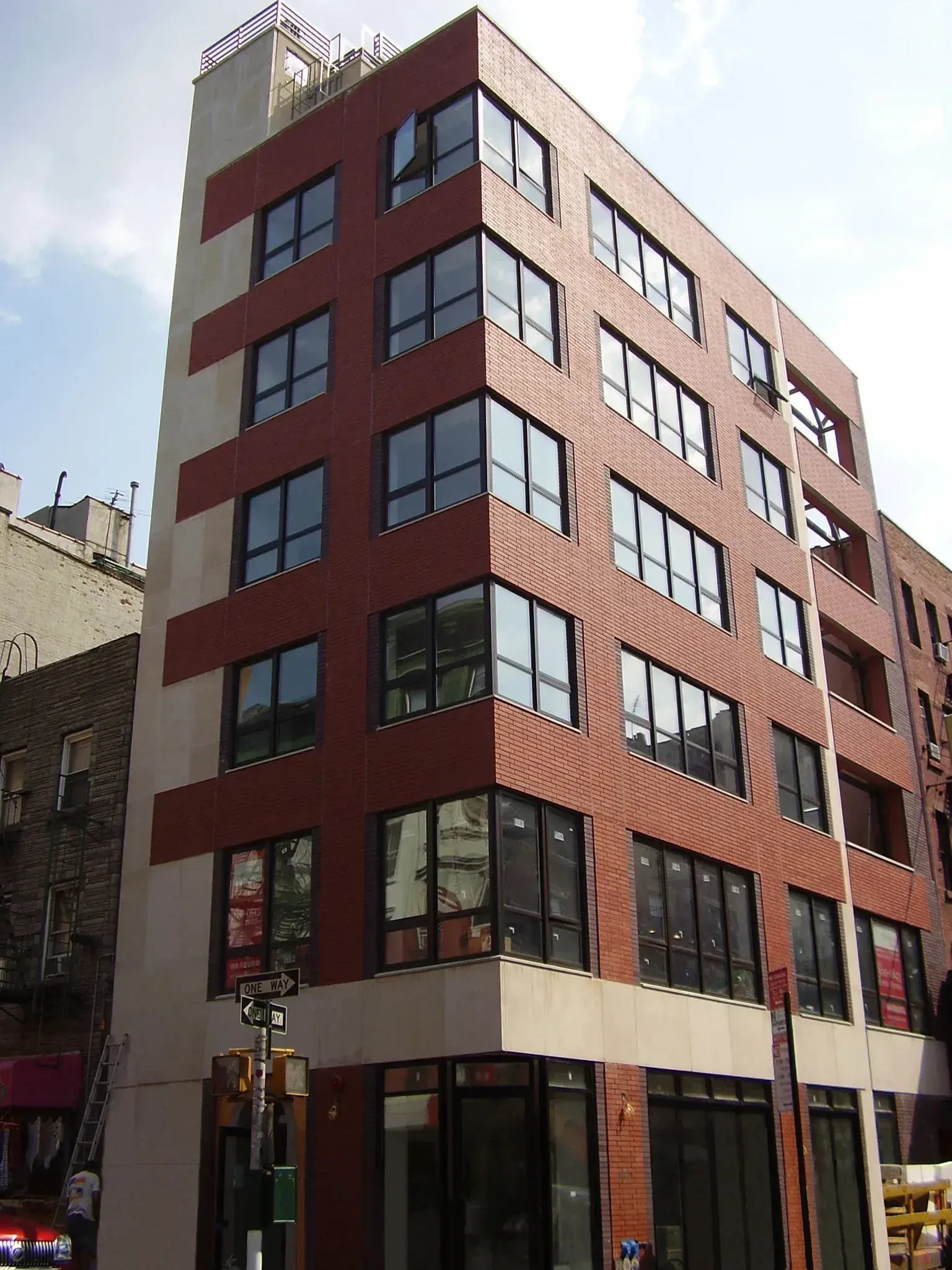 Modern brick apartment building on a city corner. Red brick facade with white stripes. Clear glass windows.