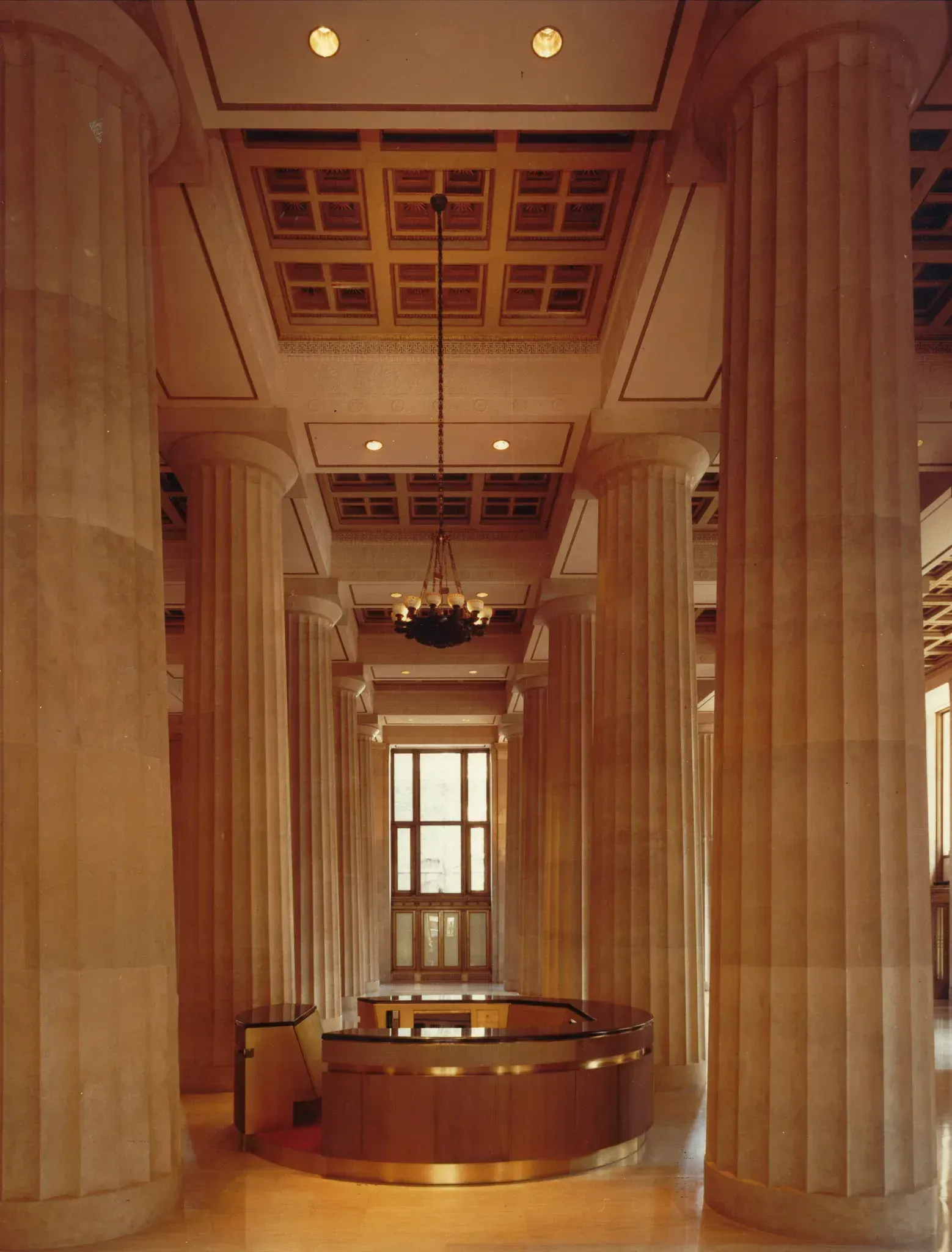 Interior view of a building with large, beige columns and a circular, gold-trimmed structure in the center.