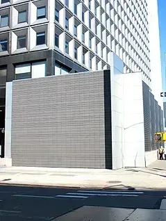 Gray-tiled wall structure in front of a tall, modern office building. Street view with a crosswalk in the foreground.