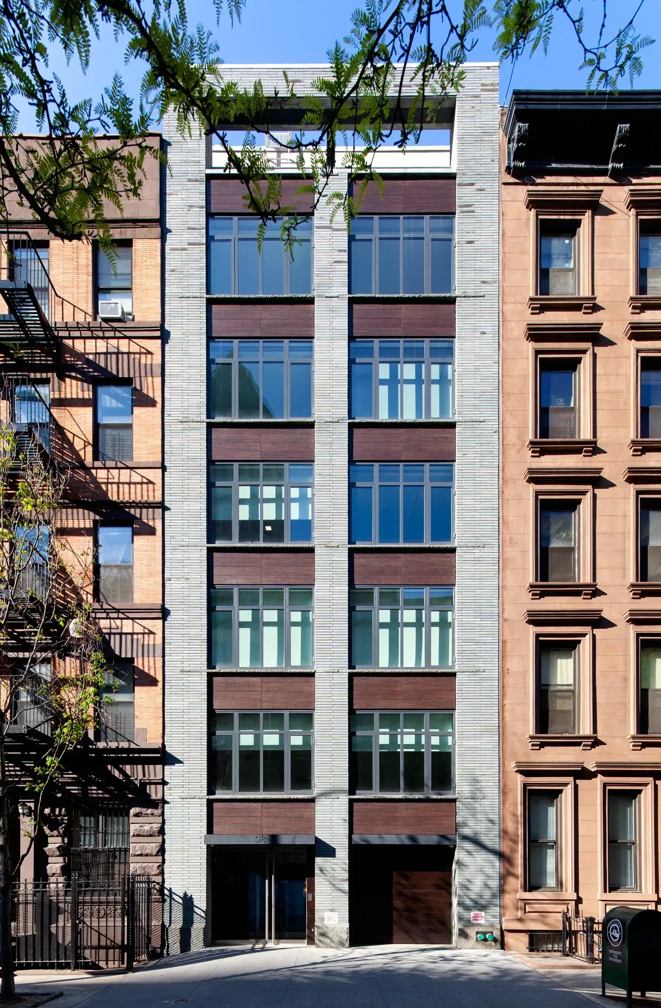 Modern six-story building with a gray stone facade between two brownstone buildings.