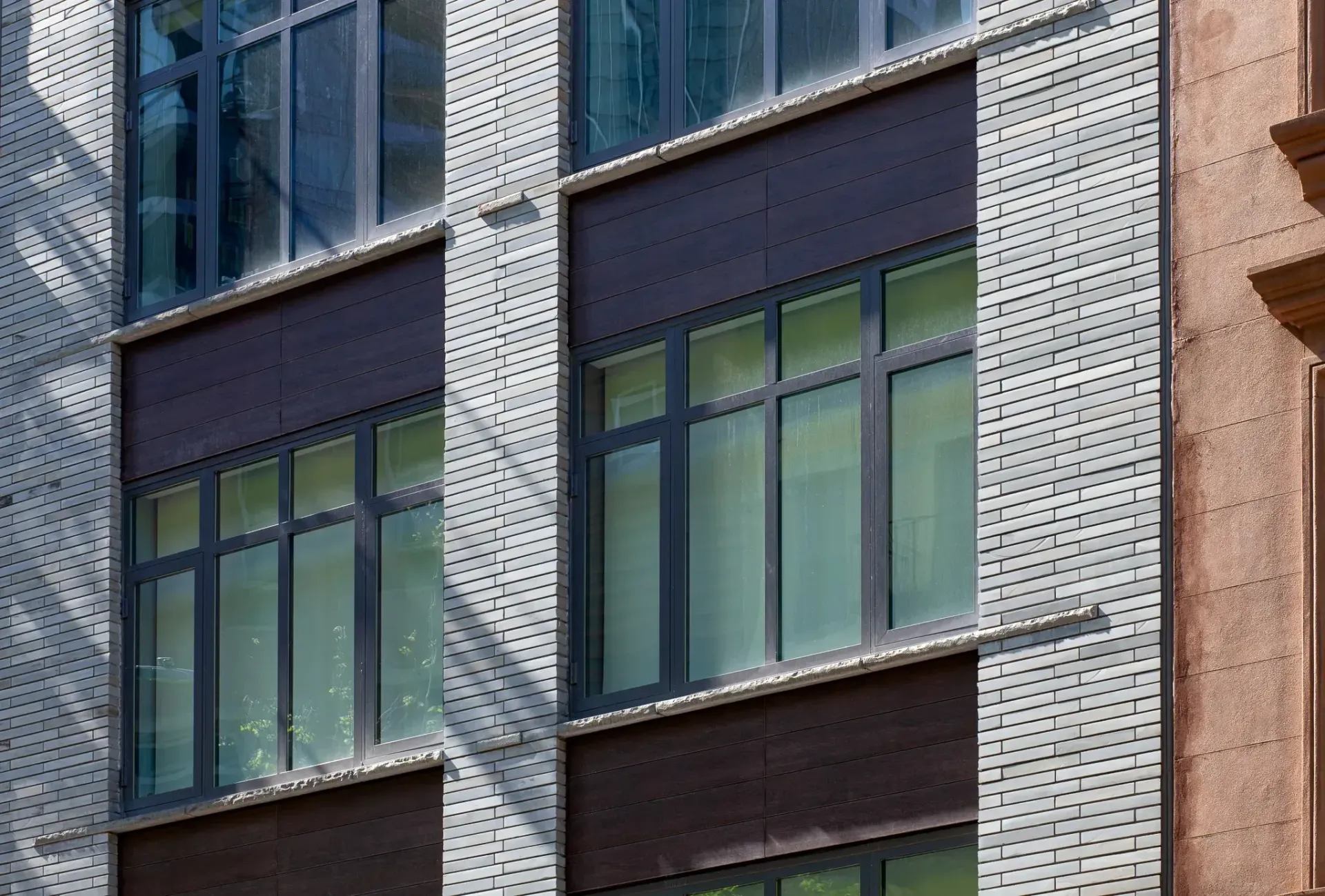 Modern building facade with windows framed by dark brown panels and perforated metal siding.