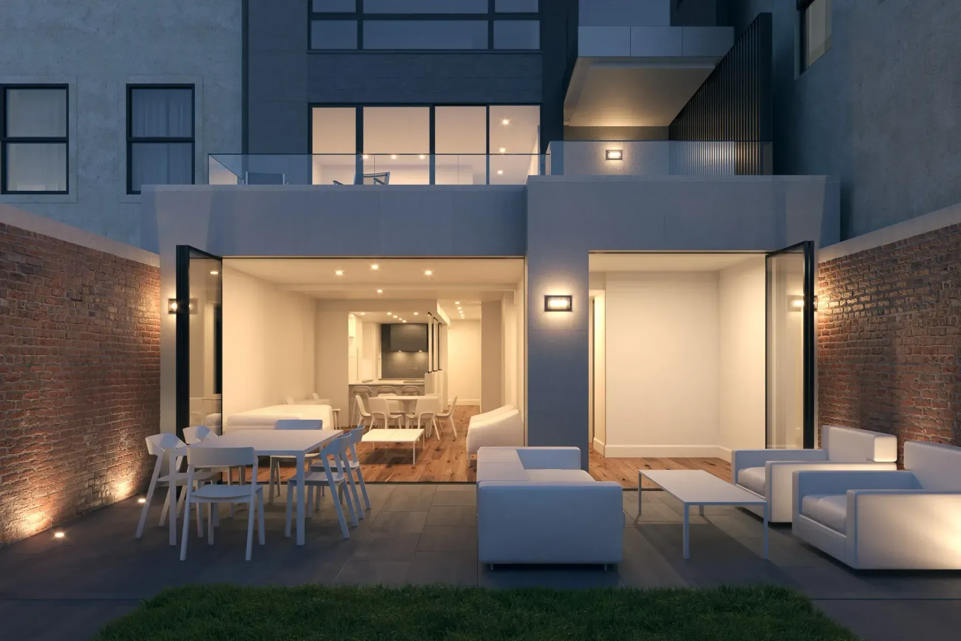 Backyard patio at dusk with outdoor seating, open doors to a modern kitchen, and brick walls.