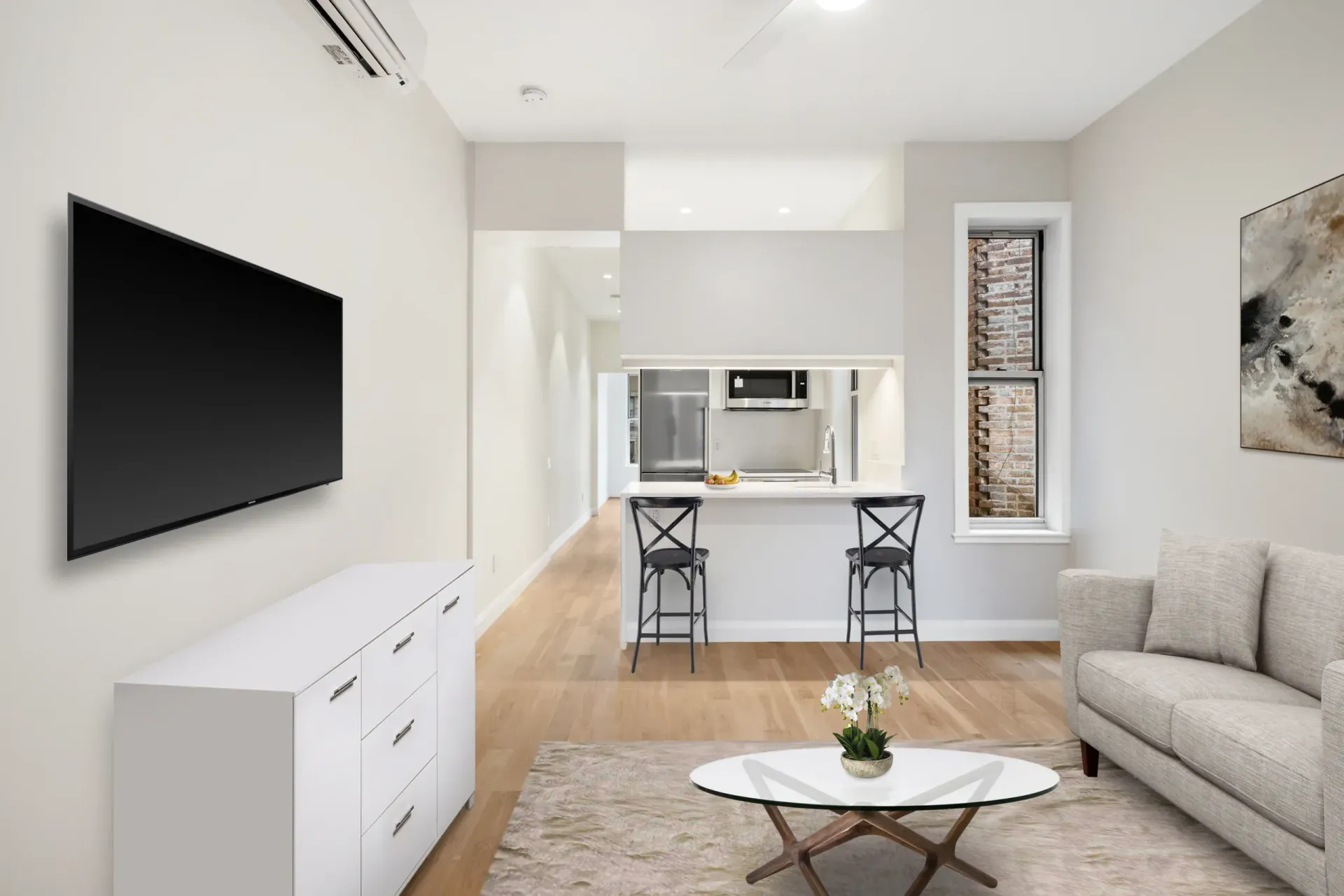 Modern living room with a TV, sofa, and kitchen. White walls and wooden floor, with a window and bar seating.