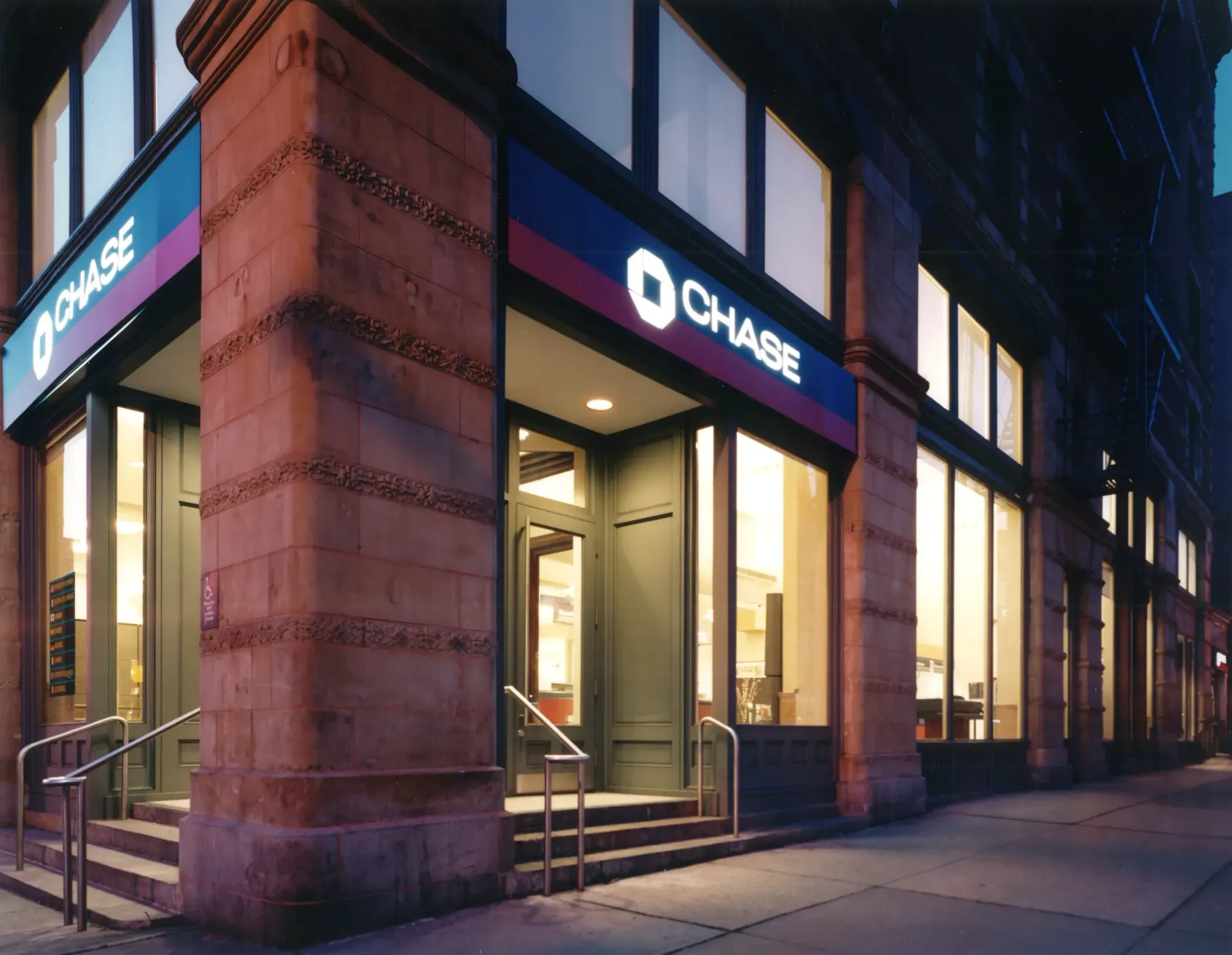 Chase bank branch on a city street corner with a blue and red sign, surrounded by stone architecture.