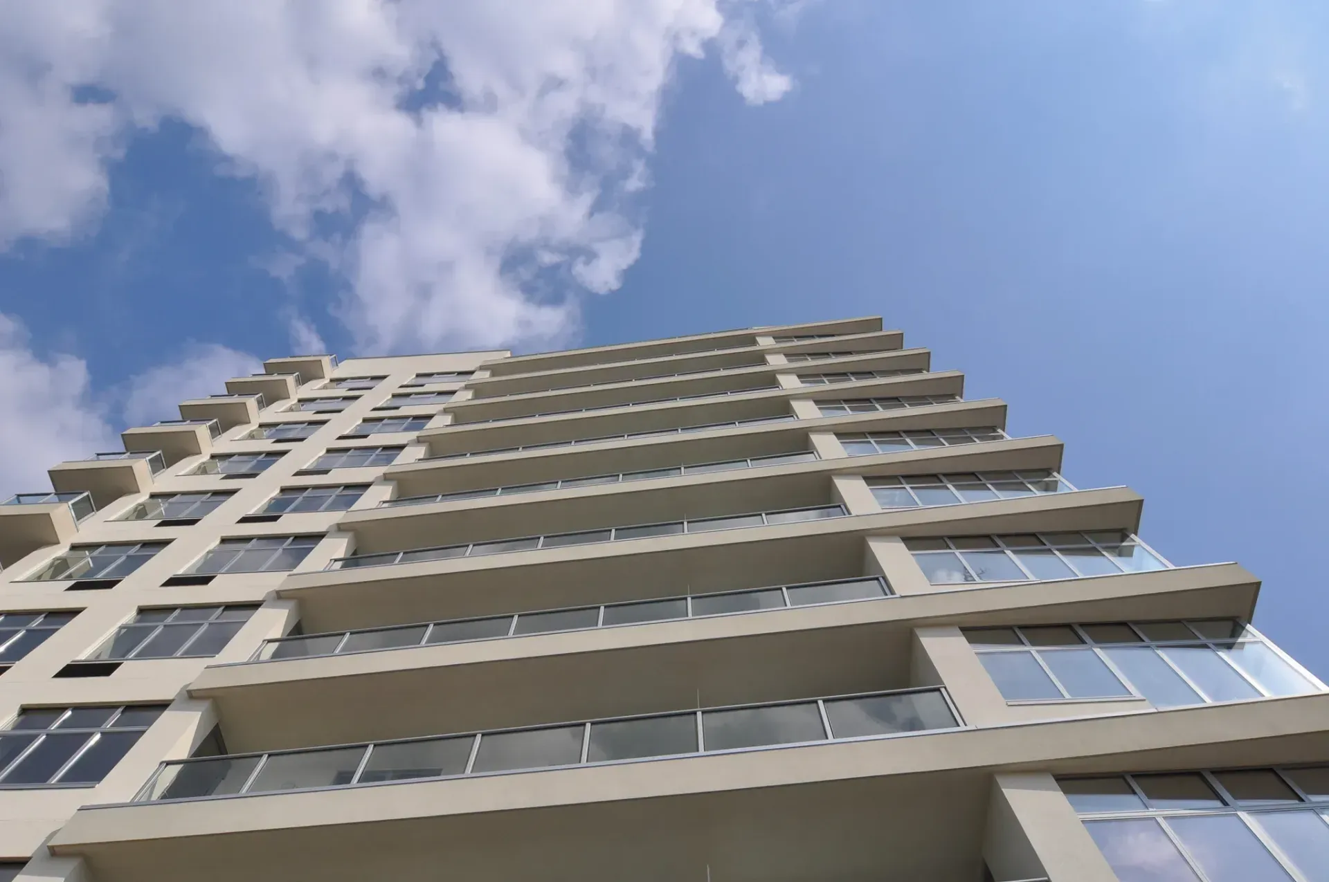 Low-angle shot of a modern white high-rise building against a blue sky with scattered clouds.