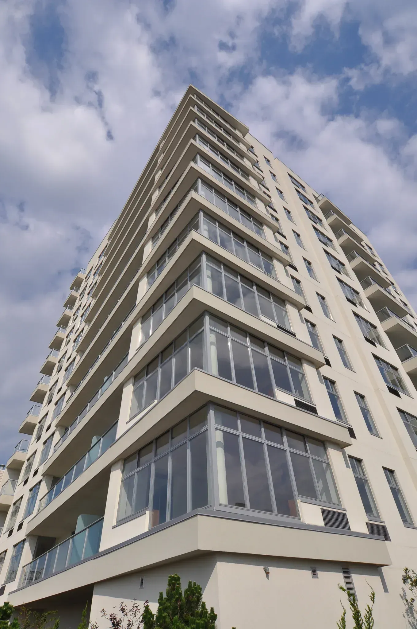Low-angle view of a tall, modern building with many balconies and large windows against a cloudy sky