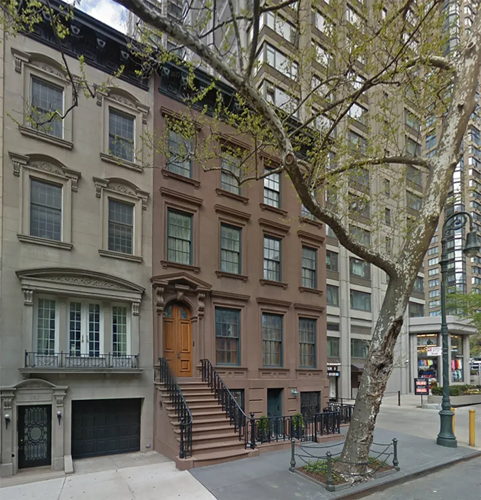 Three brownstone buildings on a city street. The center building has a wooden door and steps