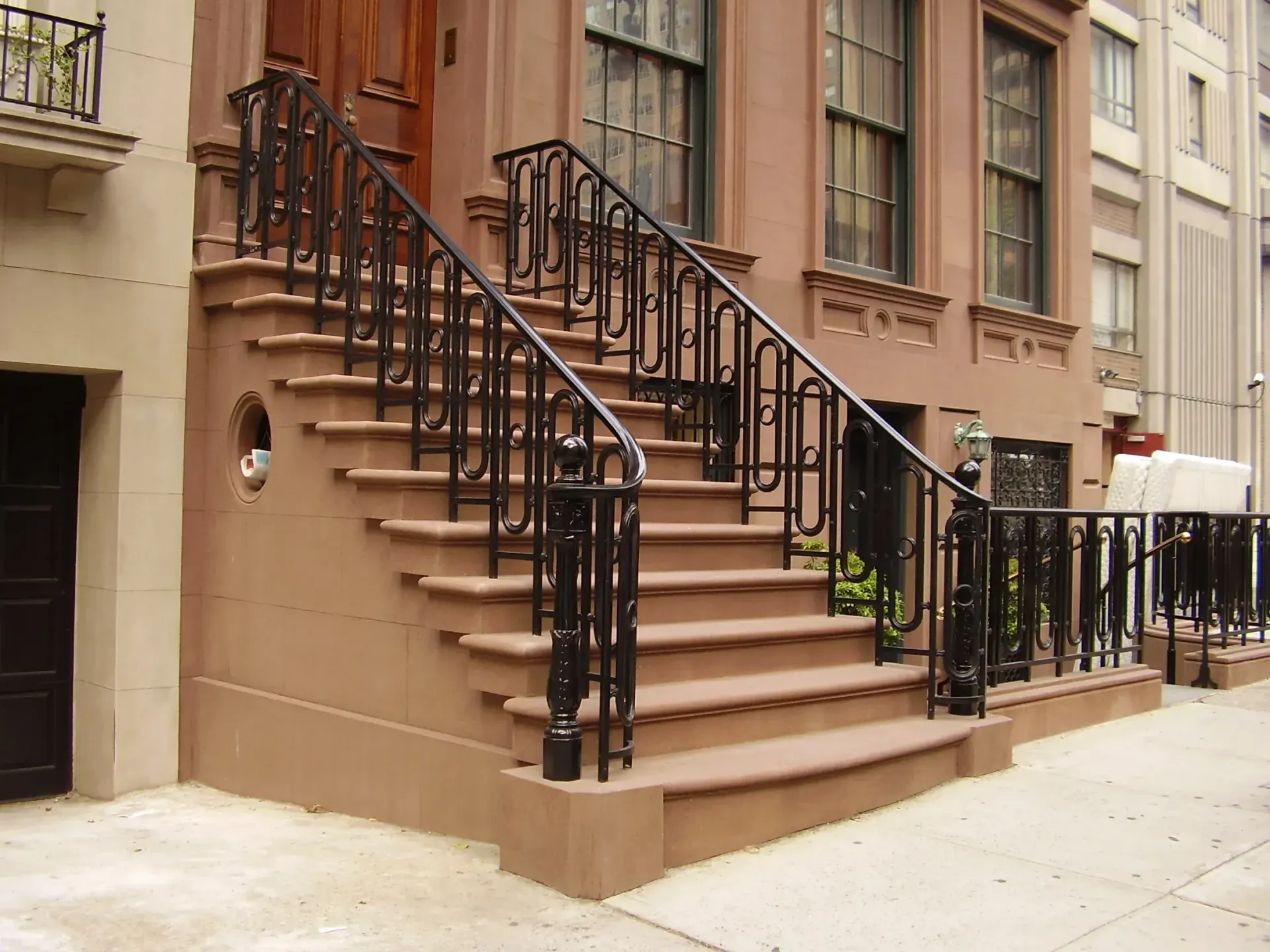 Brownstone building entrance with stairs and black wrought iron railing.