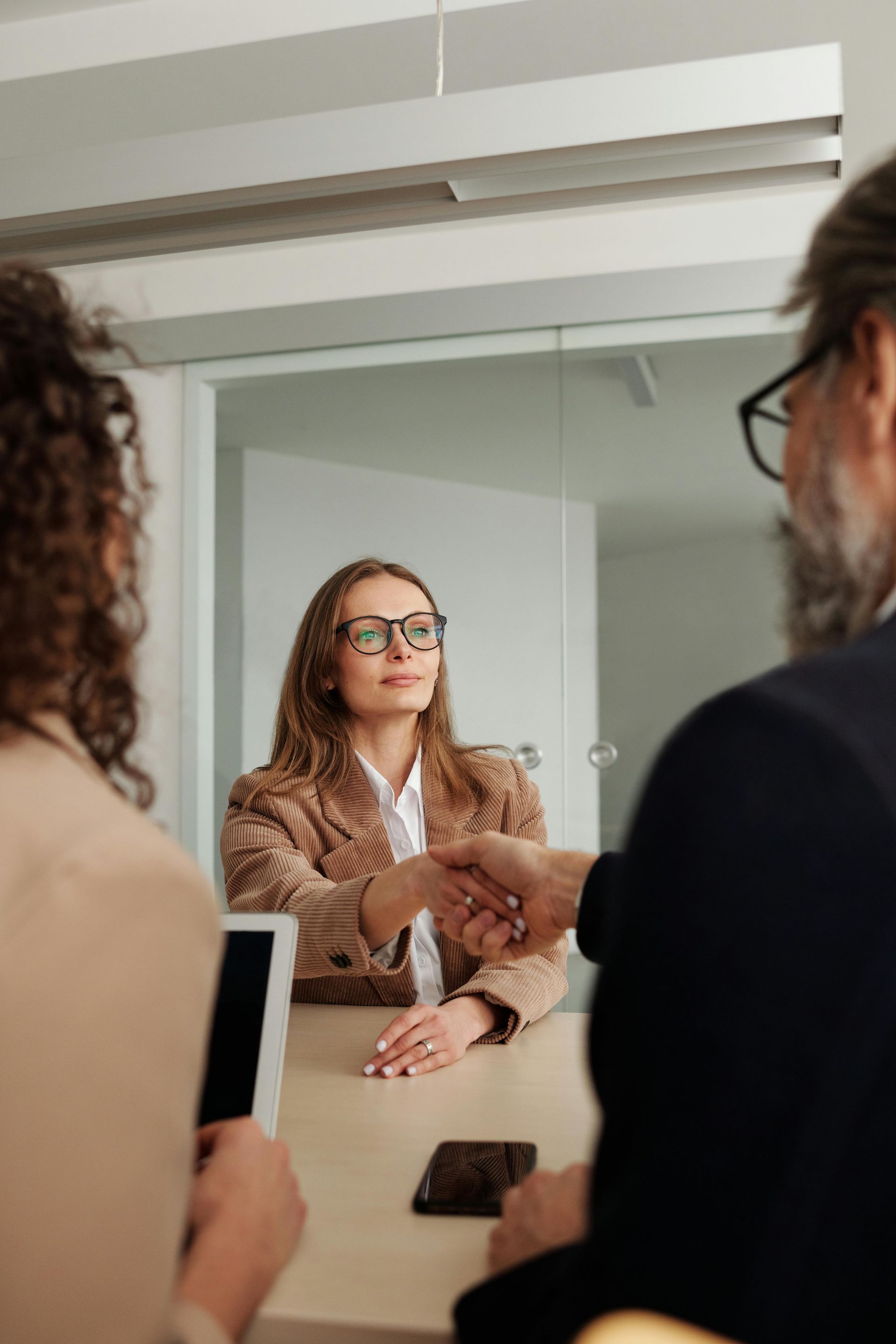 Woman in brown blazer shakes hands with a person, in an office setting.