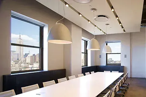 Conference room with large windows overlooking a city skyline, white table, chairs, and hanging lights.