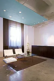 Modern office reception area with white chairs, a glass coffee table, dark brown curtains, and a blue ceiling.