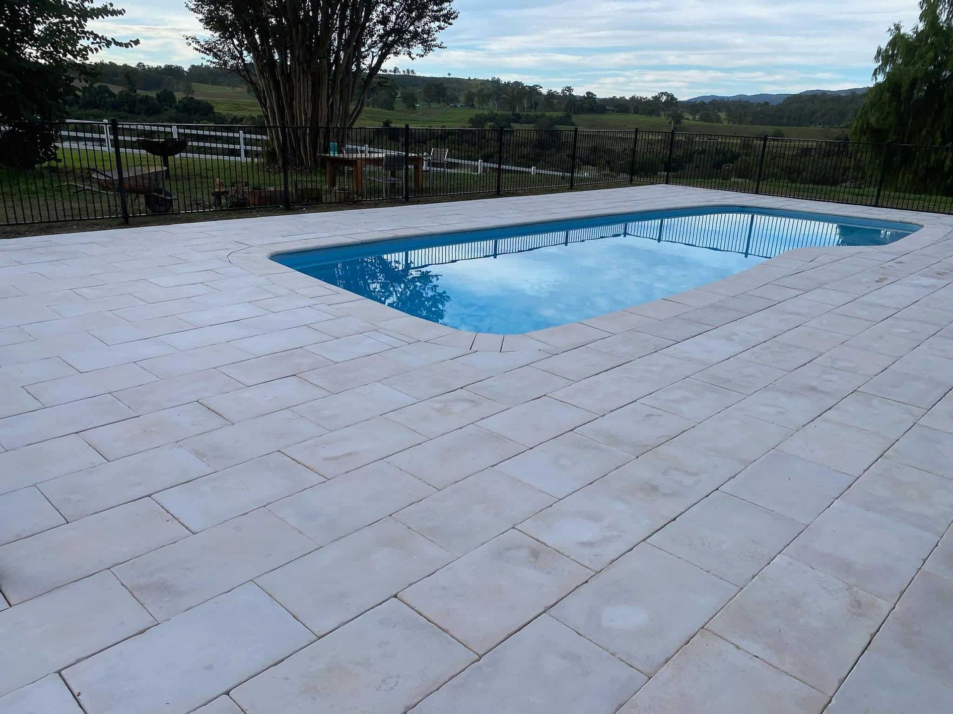 A Large Swimming Pool is Surrounded by White Tiles — Jaya Rose Earthworks and Landscape Contractors In Gulmarrad, NSW