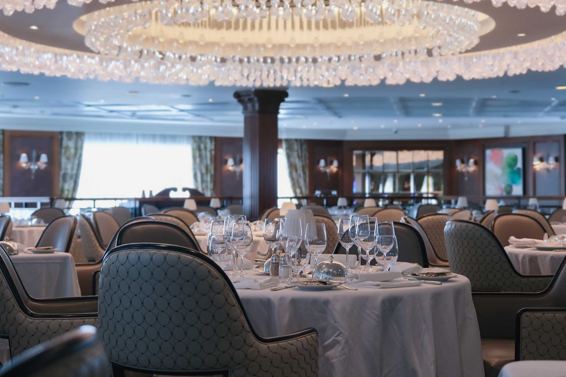 Country club dining room with crystal chandelier and formally set tables.