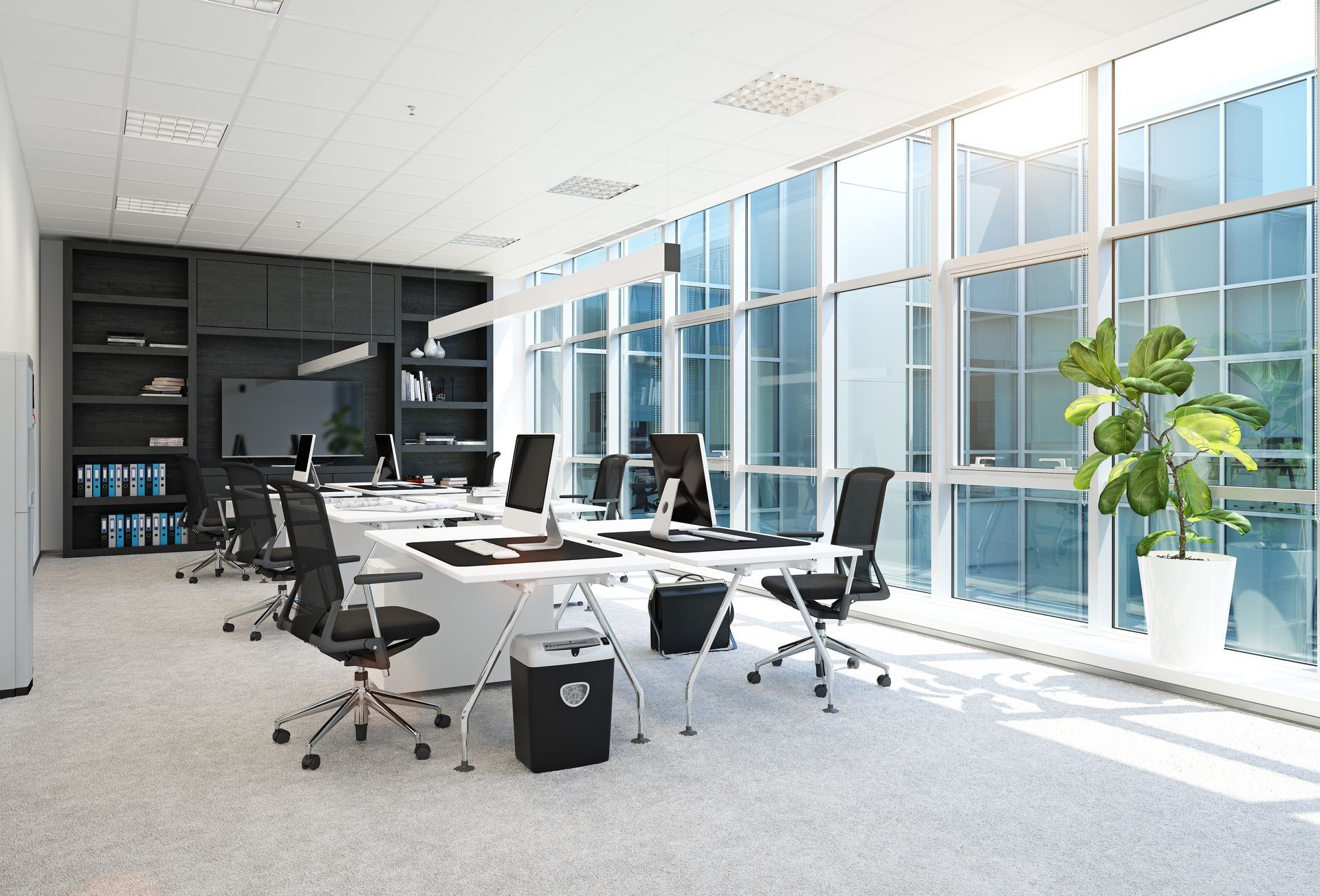 Modern office space with desks, chairs, and large windows. Black and white decor, bright natural light.