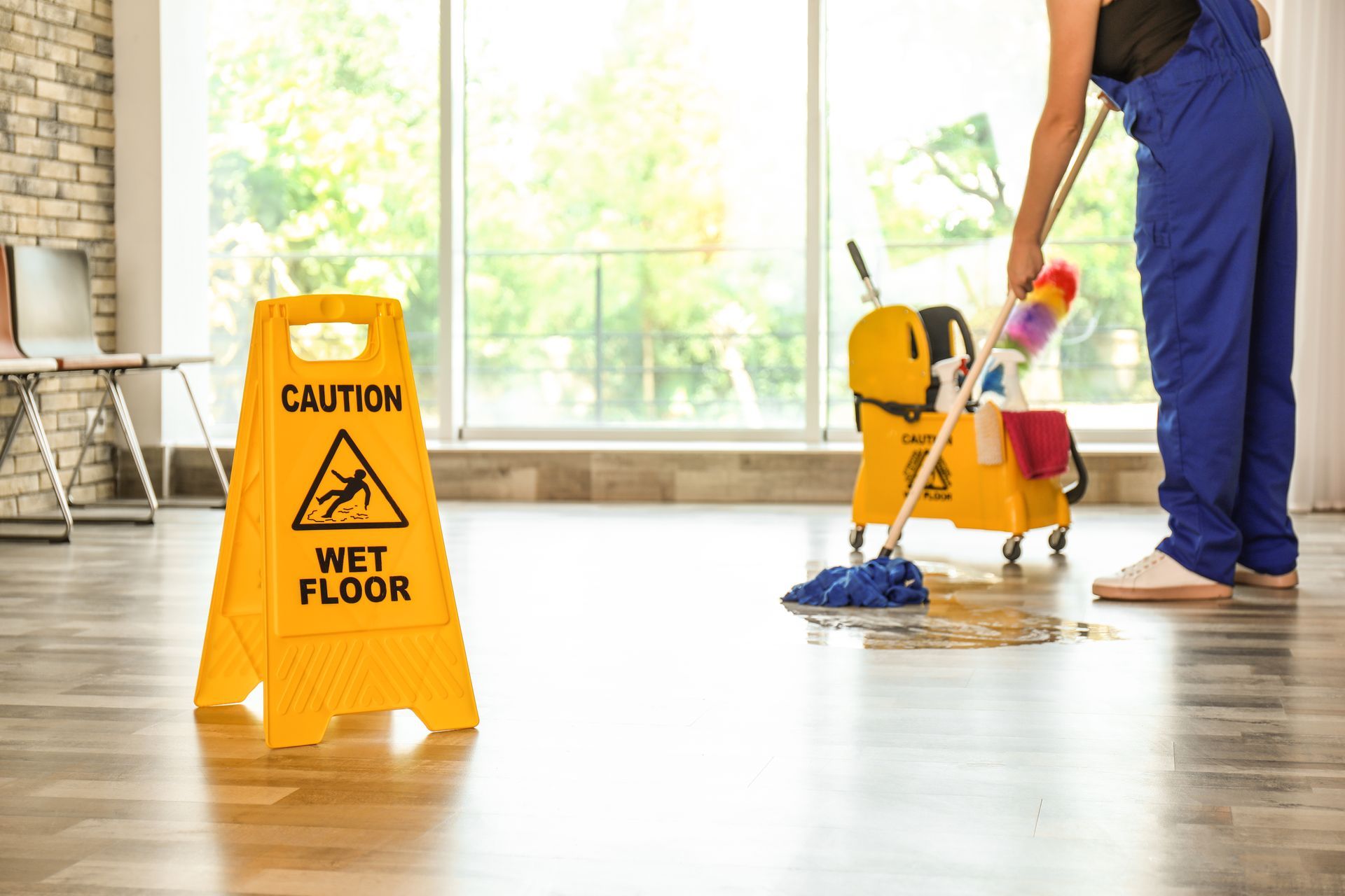 Janitorial service worker mopping floor with caution wet floor sign in clean office space.